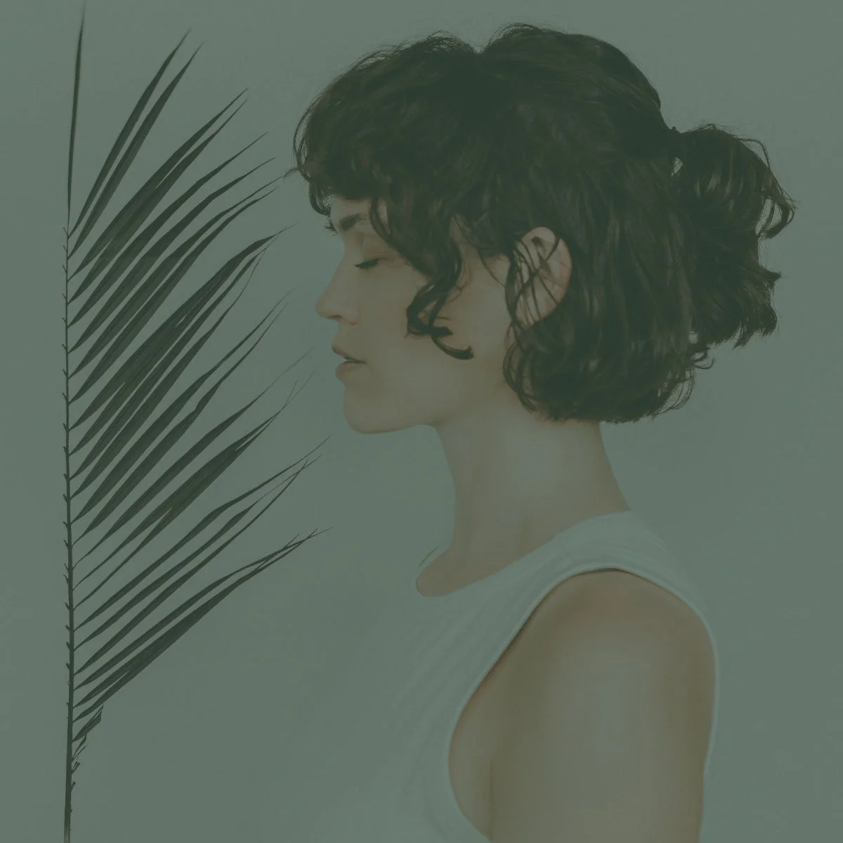A woman with short curly dark hair is shown in profile, with her eyes closed, wearing a white sleeveless top, and a large green palm leaf is partially visible on her left side.