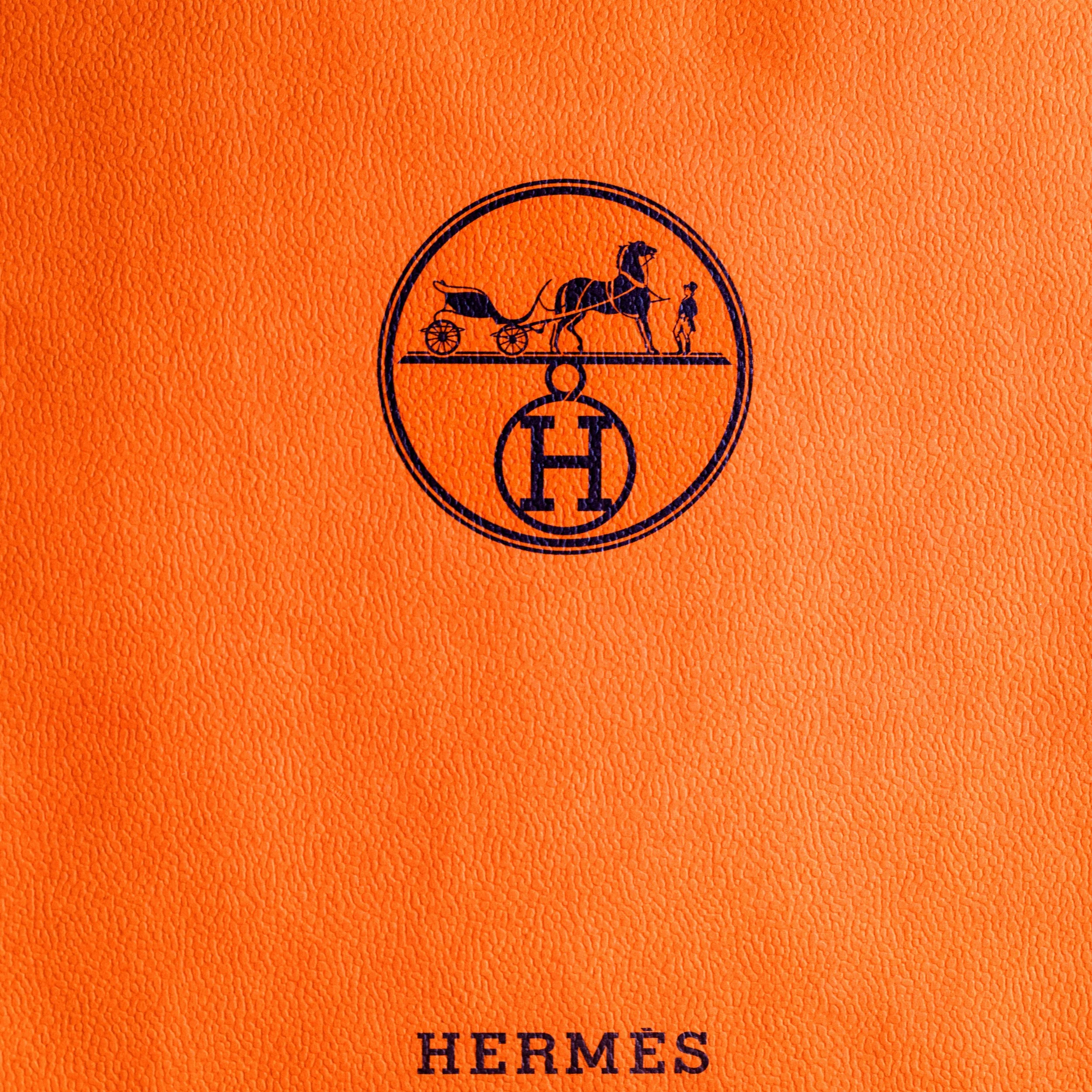 Orange textured surface with Hermès logo featuring a horse-drawn carriage and a rider, and the word "Hermès" written below.