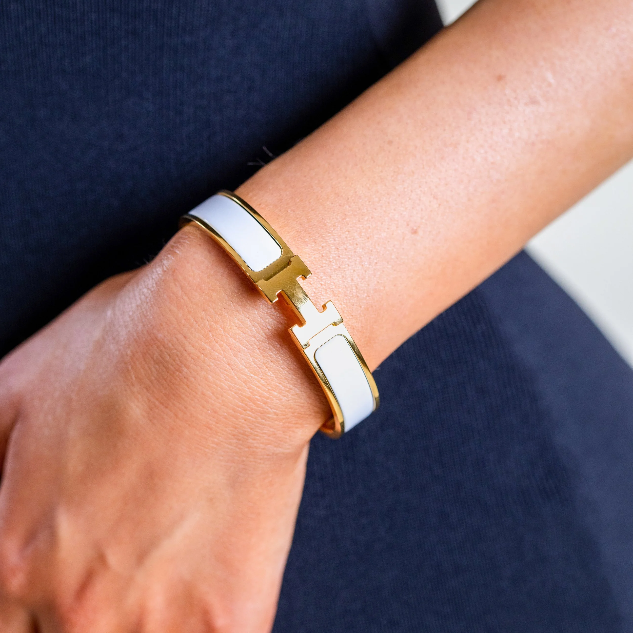 Close-up of a gold and white bracelet on a person's wrist, with the person's arm resting on their lap, wearing dark blue clothing.