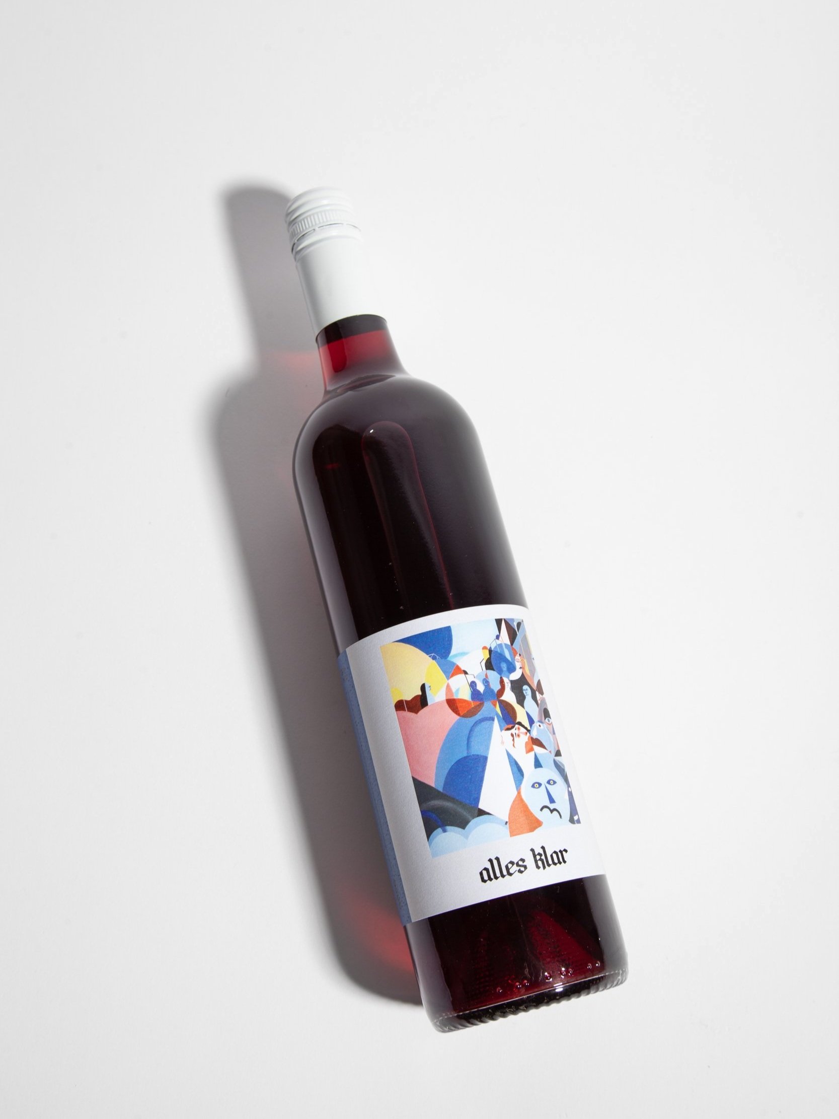 A single bottle of Alles Klar Greg Mataro 2023, is shown lying diagonally on a white surface, casting a soft shadow to its left.