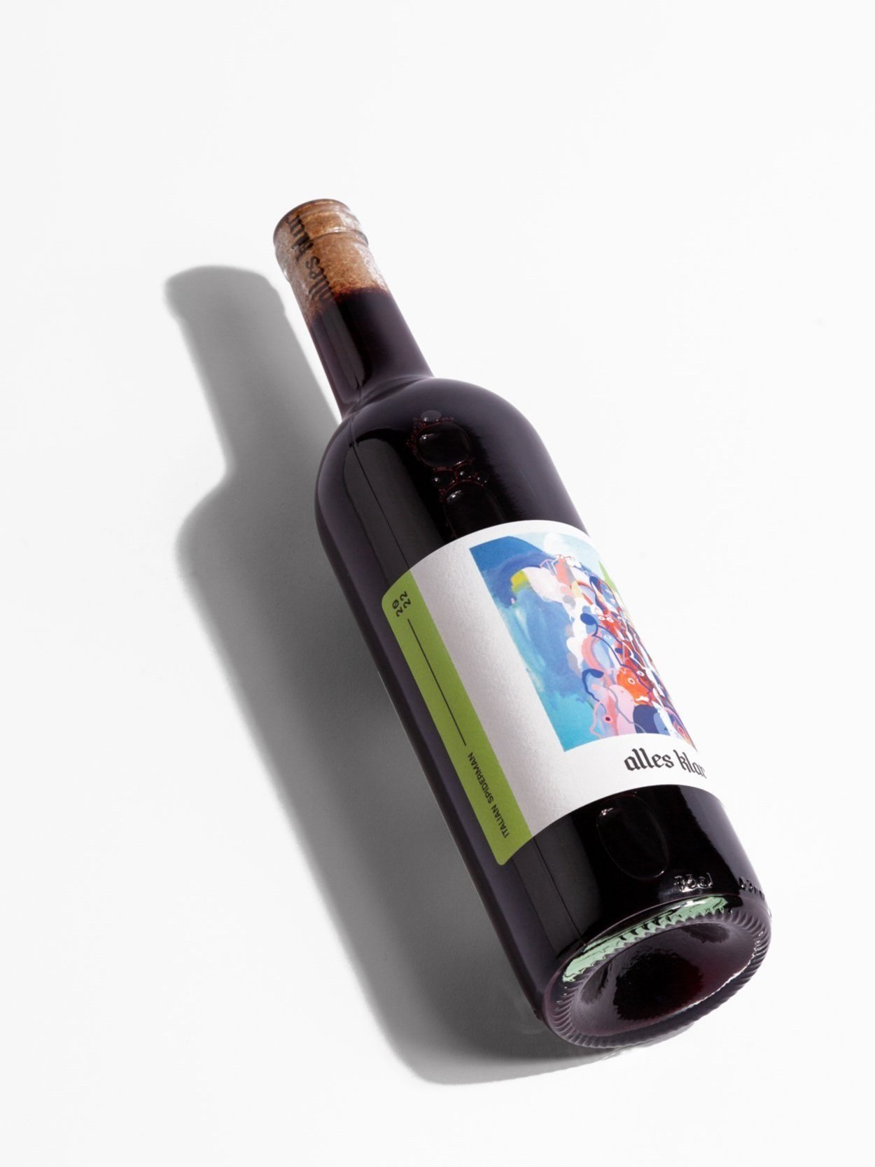 A single bottle of Alles Klar Italian Spiderman 2024, a dry red Lambrusco, is shown lying diagonally on a white surface, casting a soft shadow to its left.