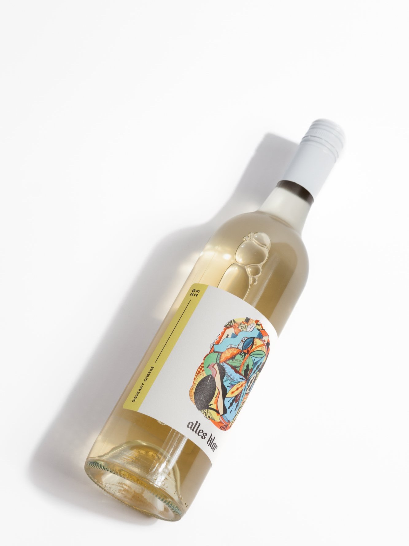 A single bottle of Alles Klar Squeaky Cheese 2023 Riverland Vermentino, a crisp dry white, is shown lying diagonally on a white surface, casting a soft shadow to its left.