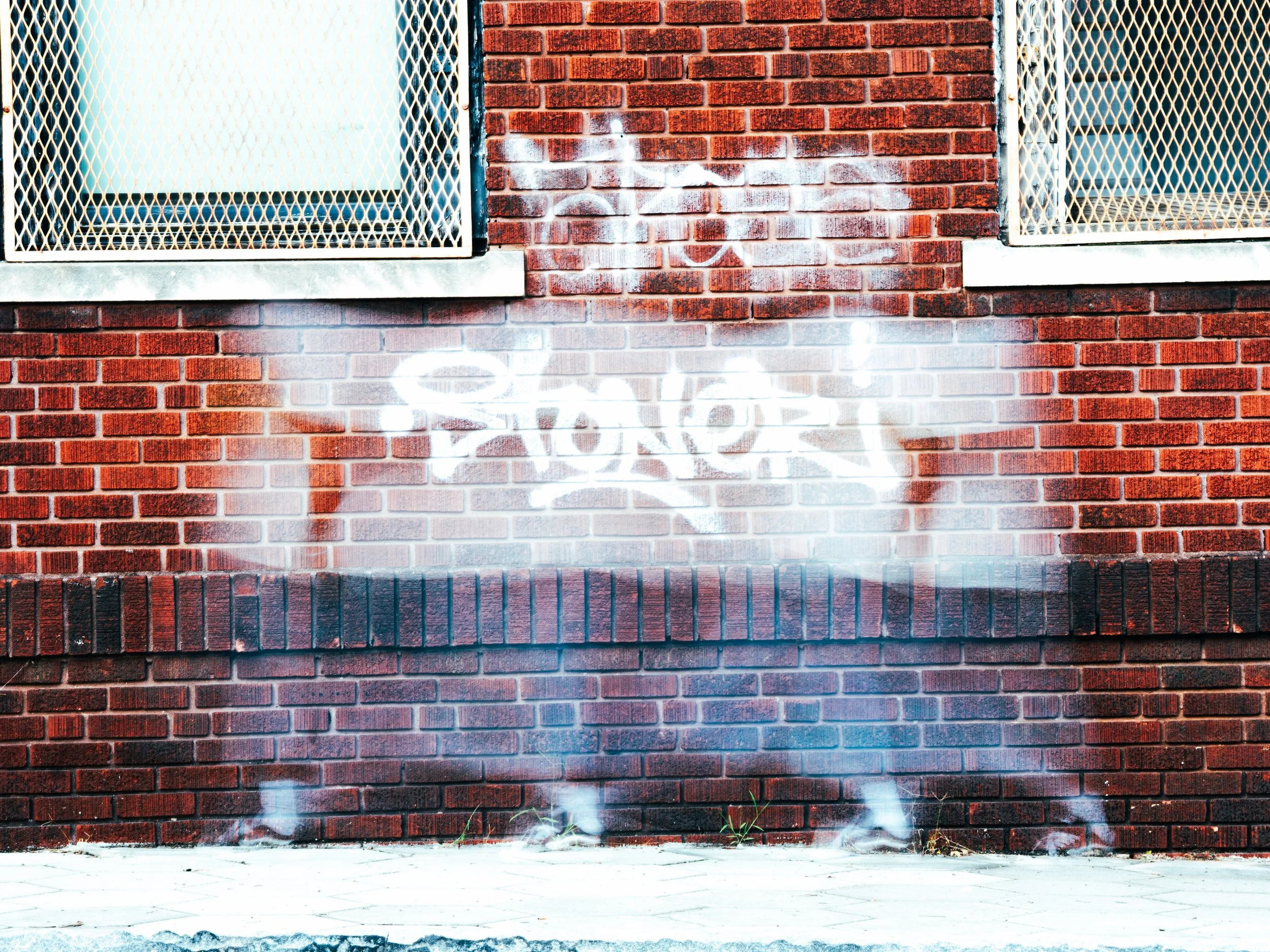 Red brick wall with two windows and white graffiti spray paint reading "LOVE" in the center.