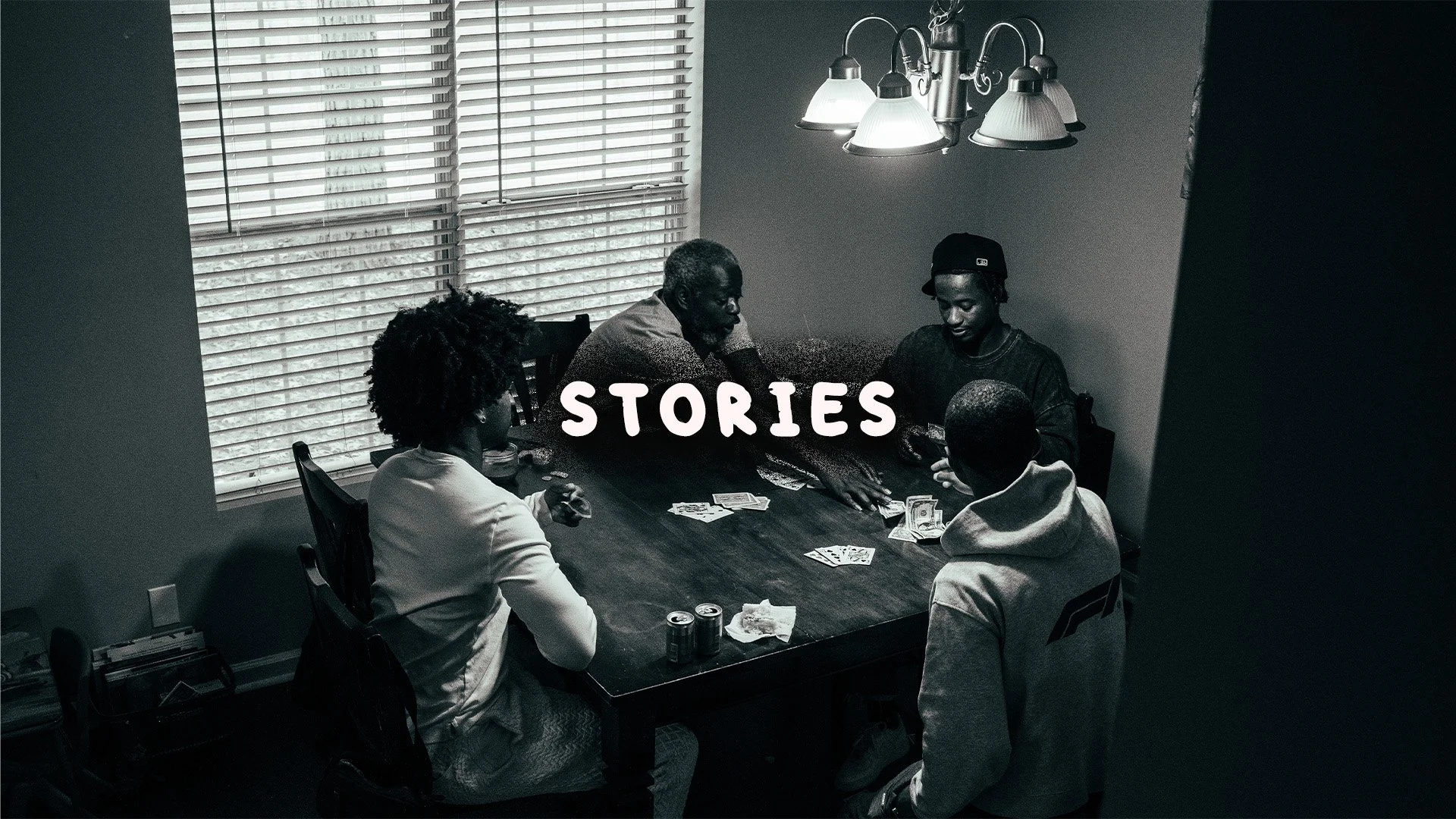 A group of five people sitting around a dining table, playing cards, with the word "STORIES" overlaid on the image.