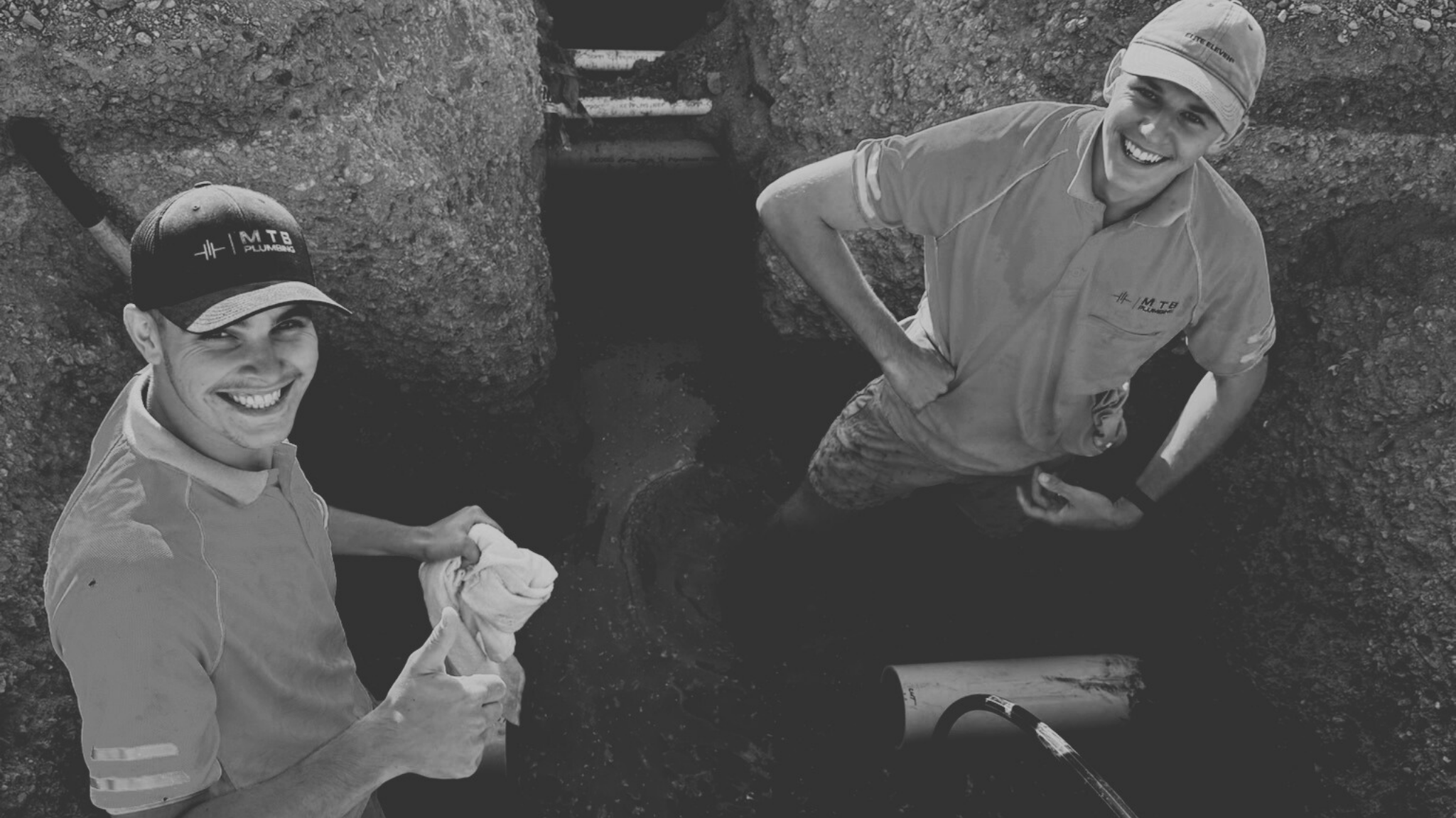 Two smiling men standing in a trench with a pipe visible. One man is wearing a cap with 'M T B Plumbing' and holding a cloth, giving a thumbs-up. The other man is wearing a cap and a company shirt, with one hand on his hip, posing confidently.