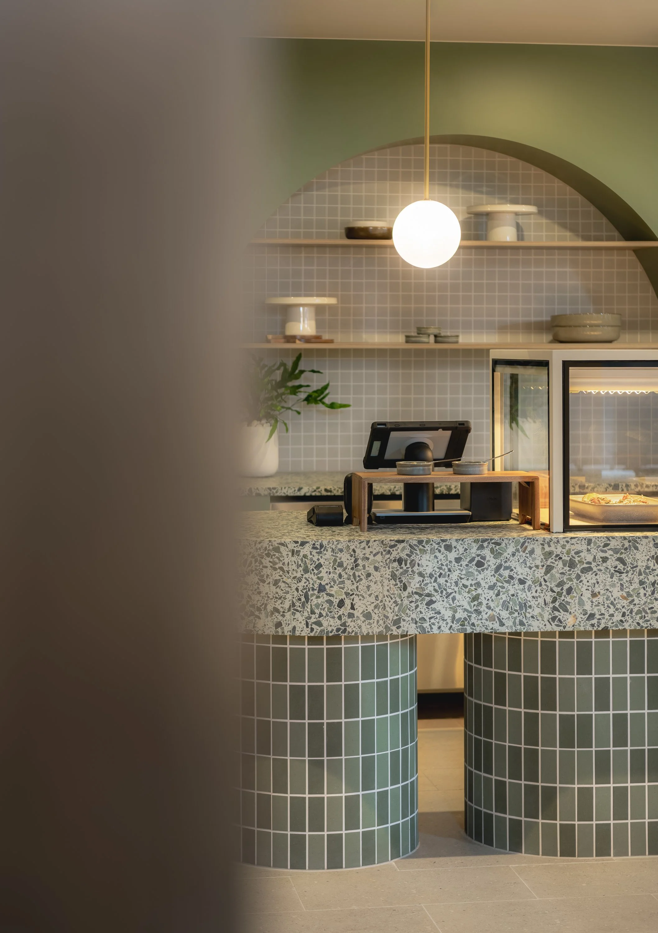 Detailed view of green tiled cafe joinery, arched wall finishes and suspended feature lighting.