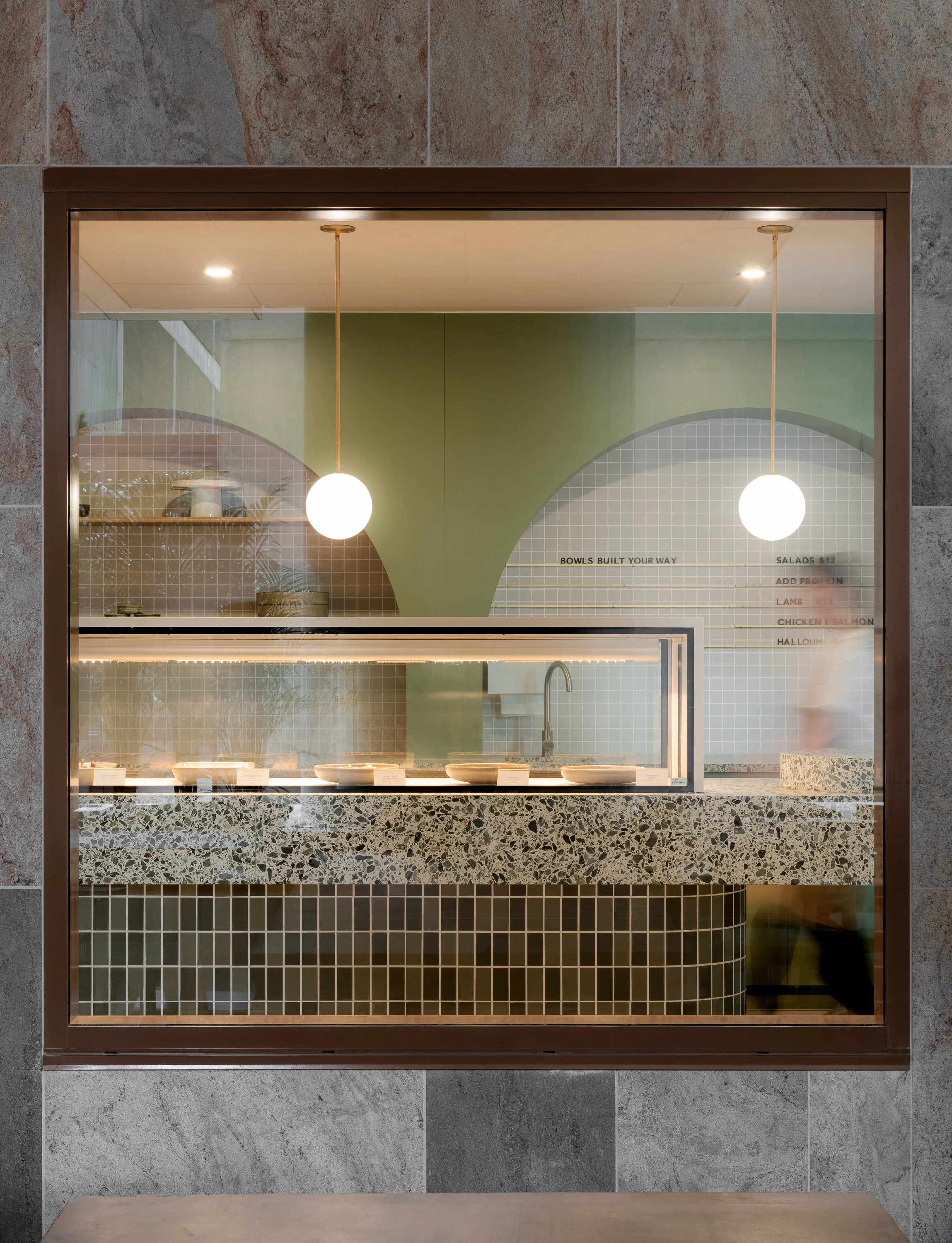 Street-facing cafe interior with terrazzo counter, green tiles and arched architectural details.