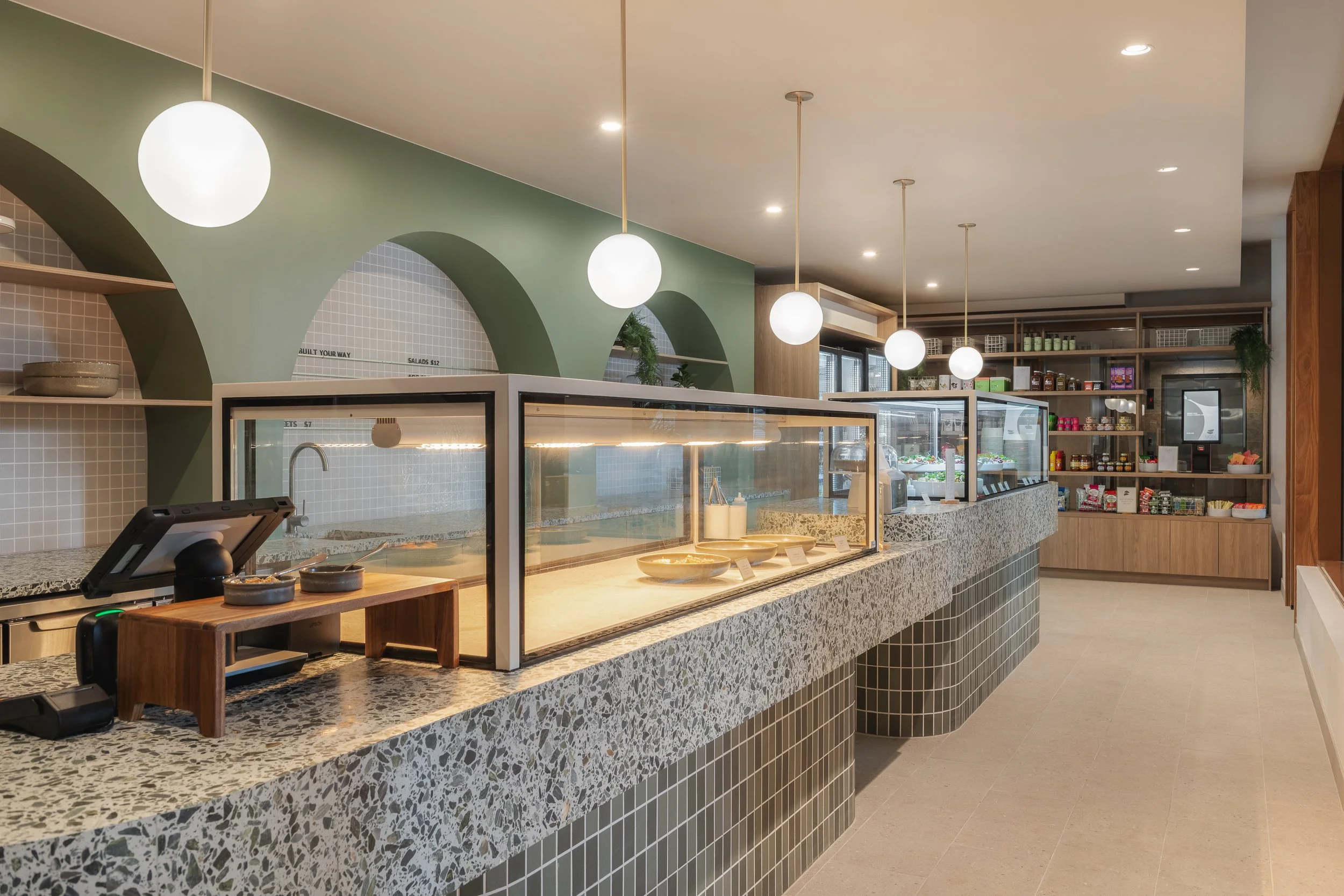 Cafe interior showcasing a curved terrazzo service counter, green tiled joinery and soft architectural arches.