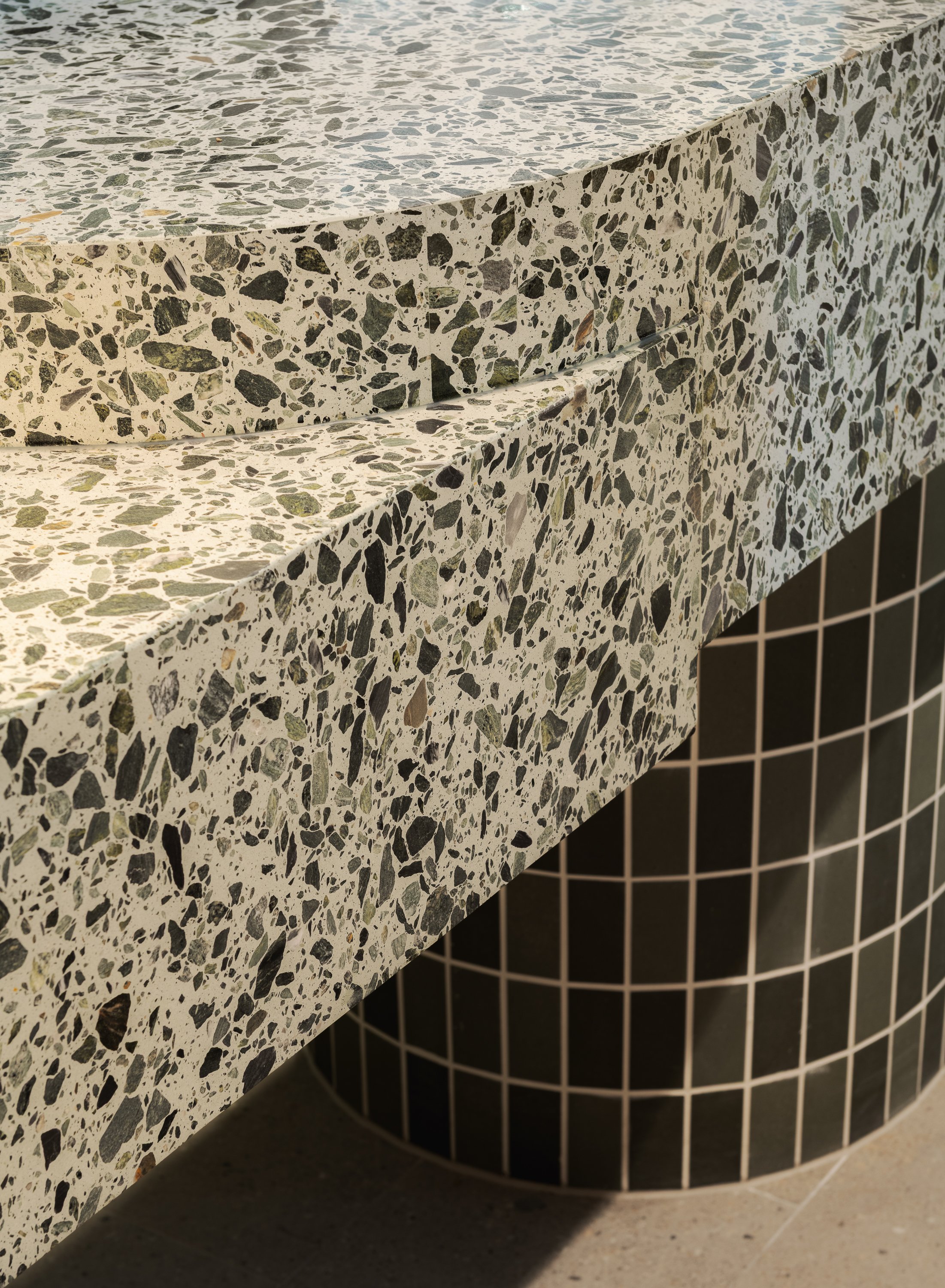 Close-up of terrazzo benchtop detailing and dark green curved tile cladding.