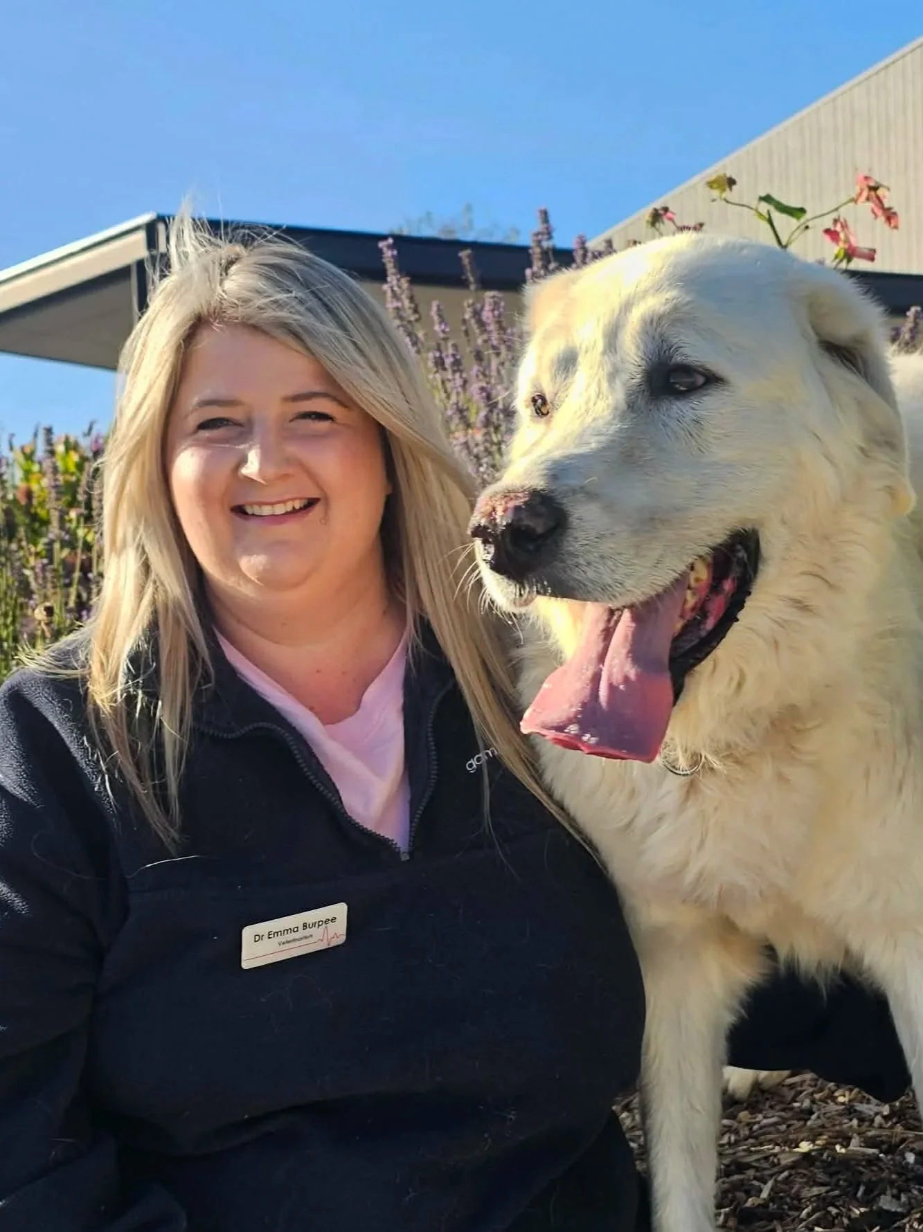 Smiling woman in a black and white sports shirt standing against a plain white wall.