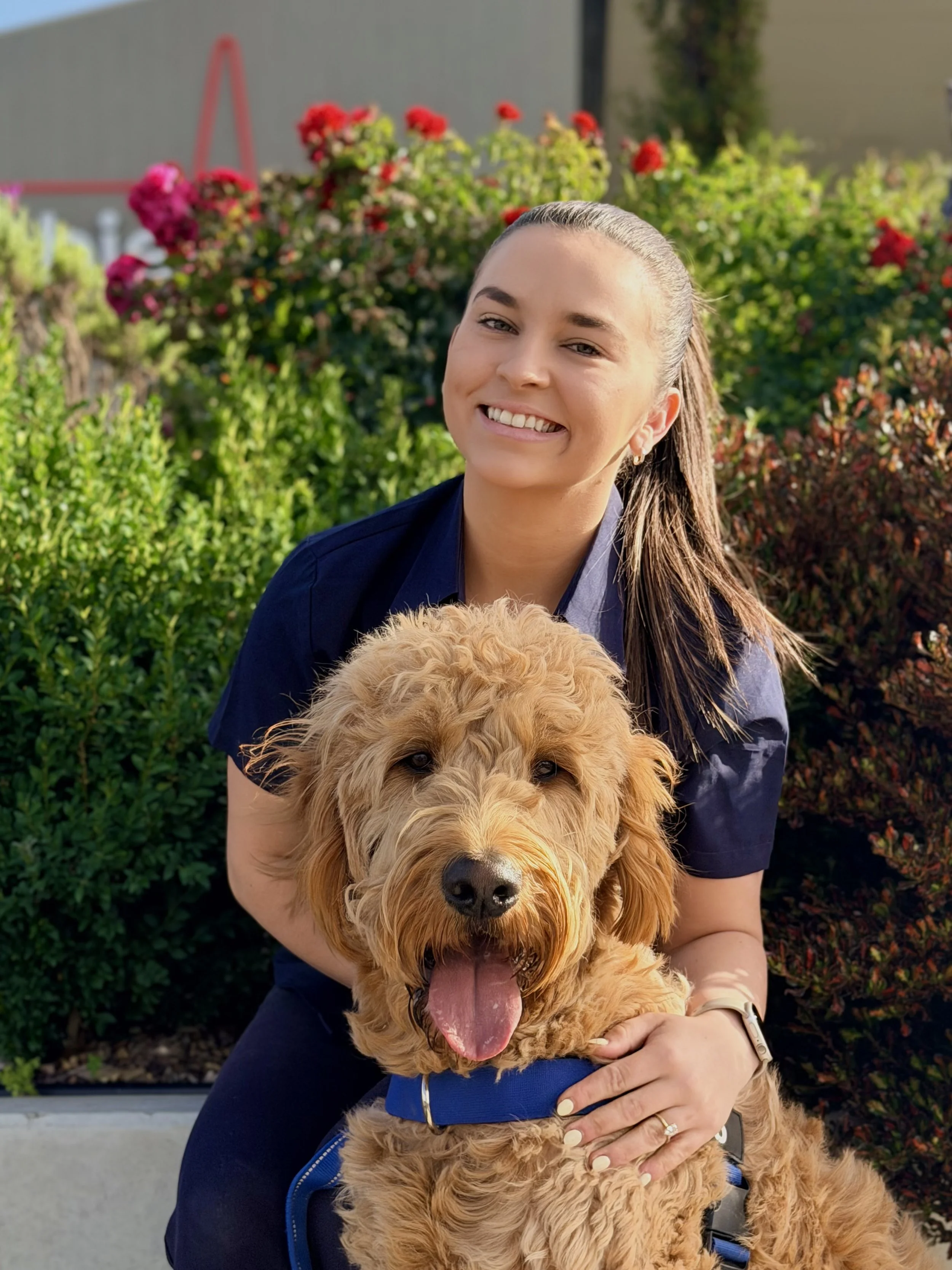 A young woman with a friendly smile, wearing a navy blue uniform vest, standing against a plain, light-colored background.