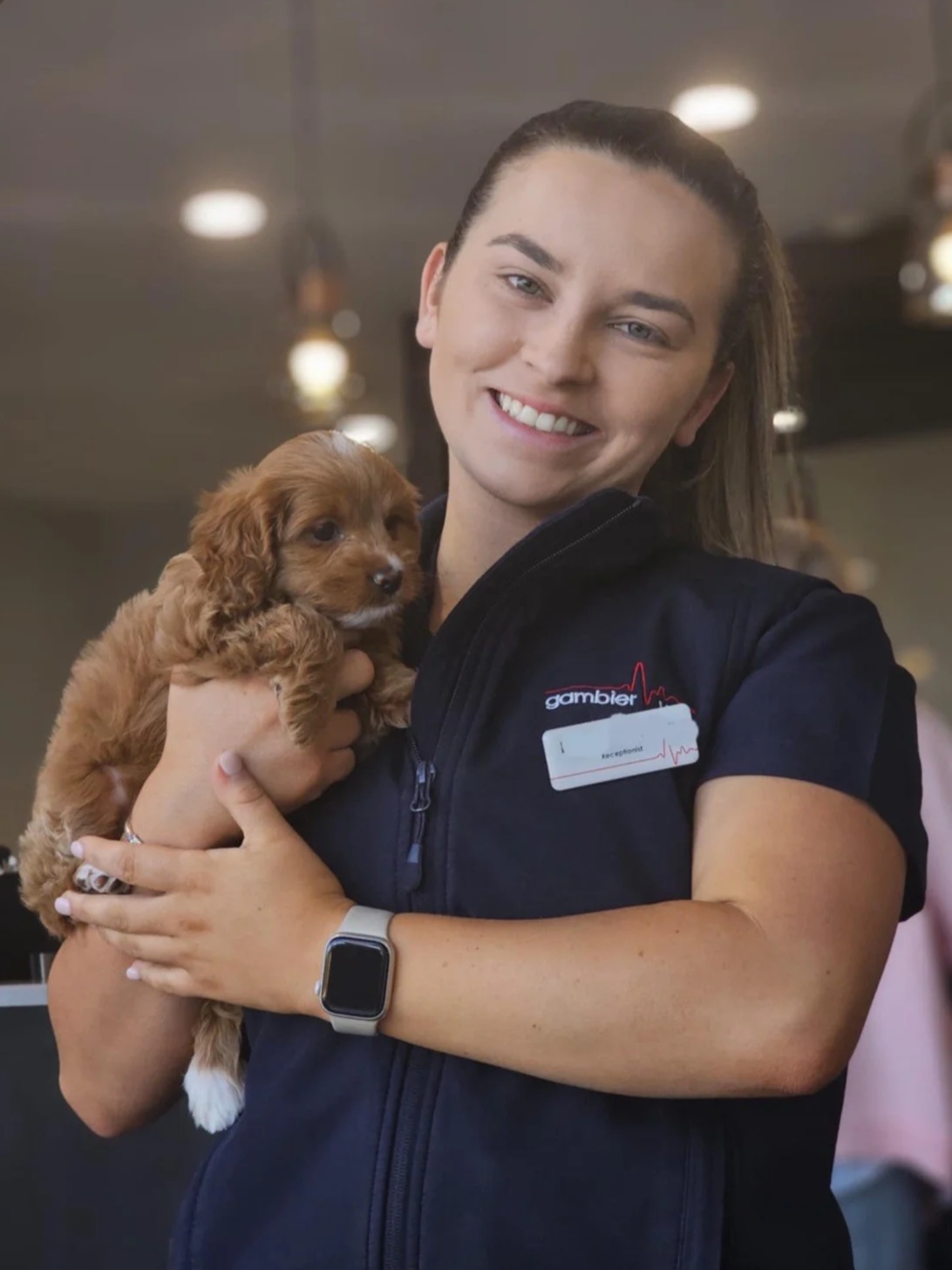 A man and woman, both in veterinary uniforms, standing outside Gambier Vets clinic during daytime.