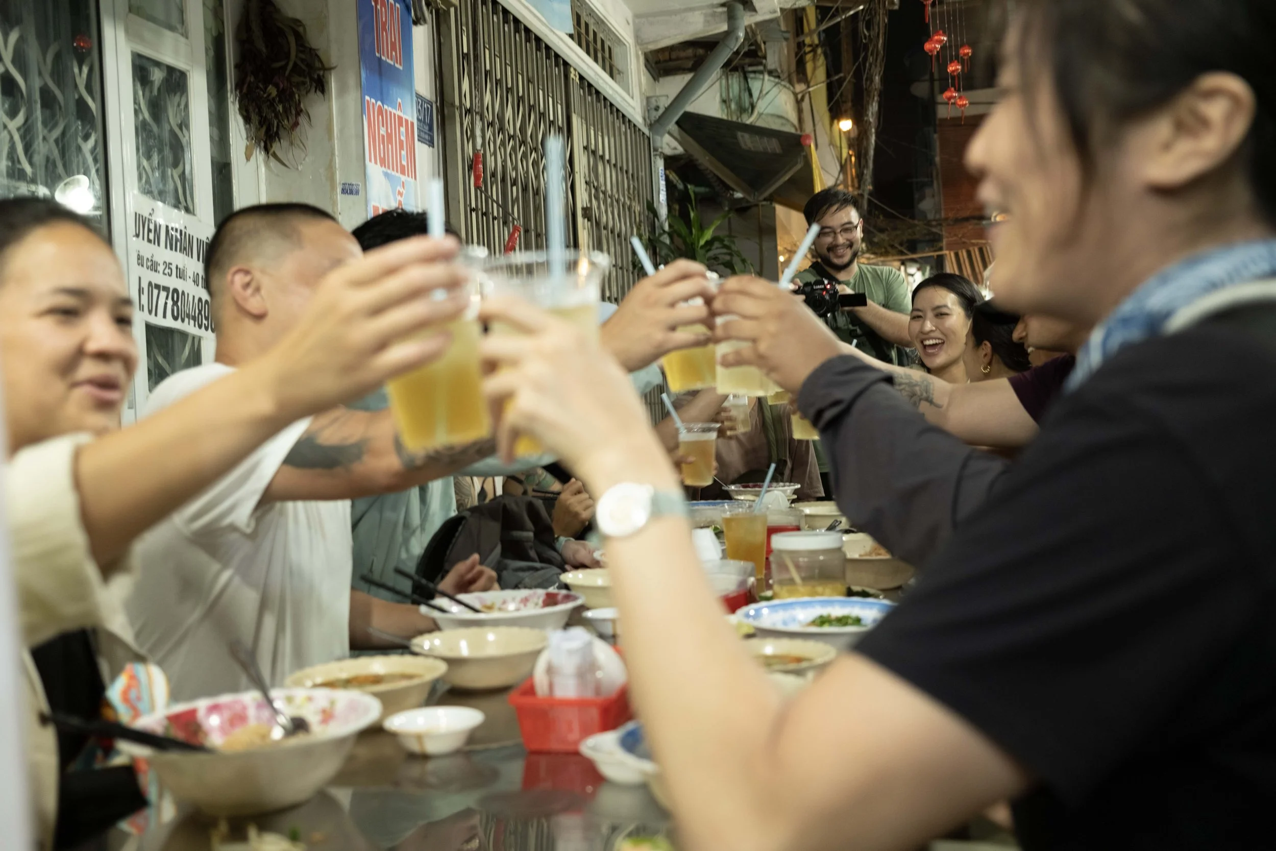 Group of people raising their glasses in a toast at a dinner party outside at night.