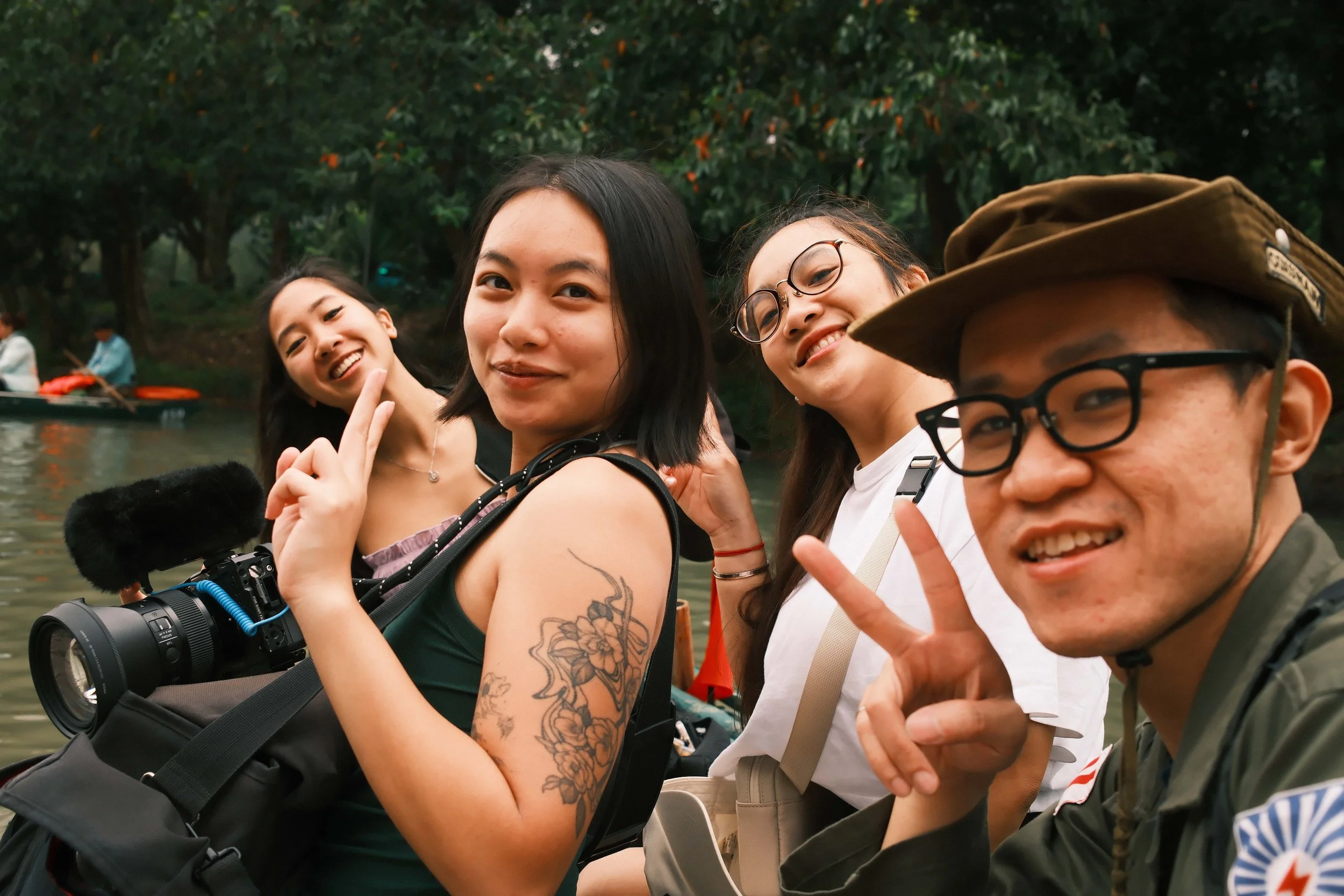 Group of five smiling young adults taking a selfie near a body of water with trees in the background.