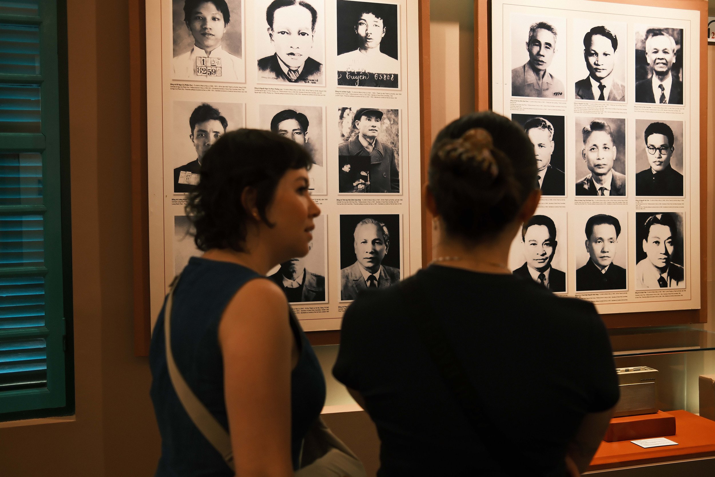 People viewing a display of black-and-white photographs of historical figures on a wall in an indoor setting.