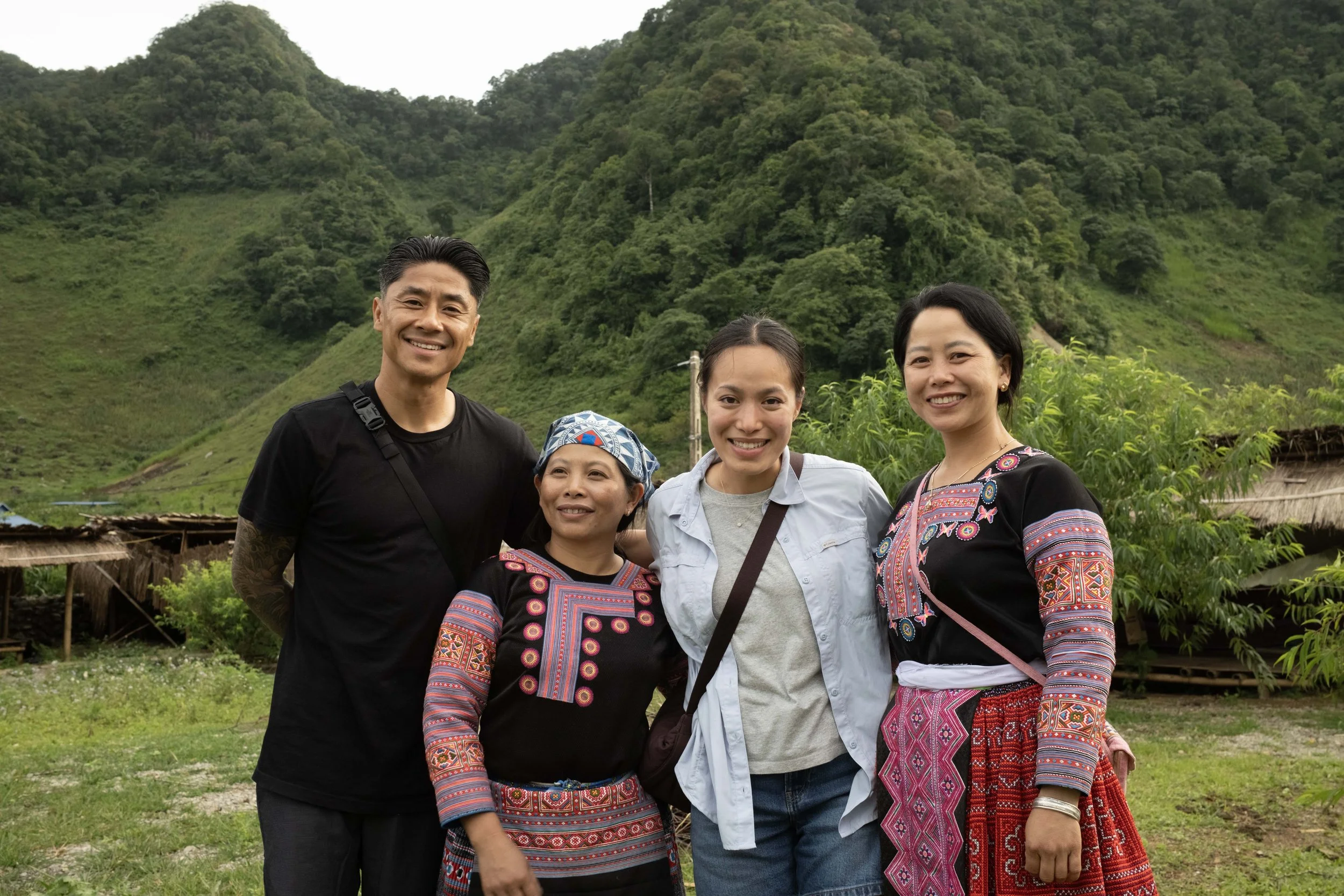 Group of five people smiling outdoors with green hills and trees behind them.