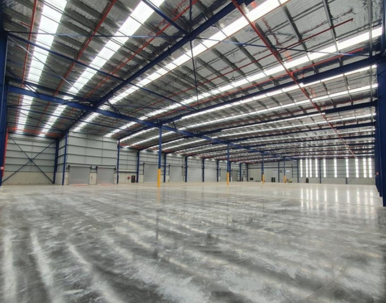 Empty warehouse interior with high ceiling, metal beams, and polished concrete floor