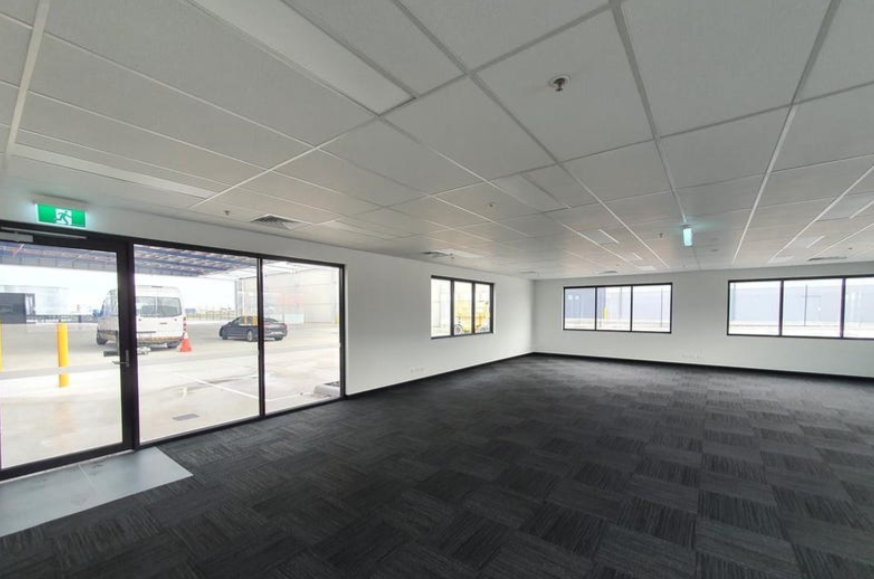 Empty office space with large windows, carpeted floor, and glass door leading outside.