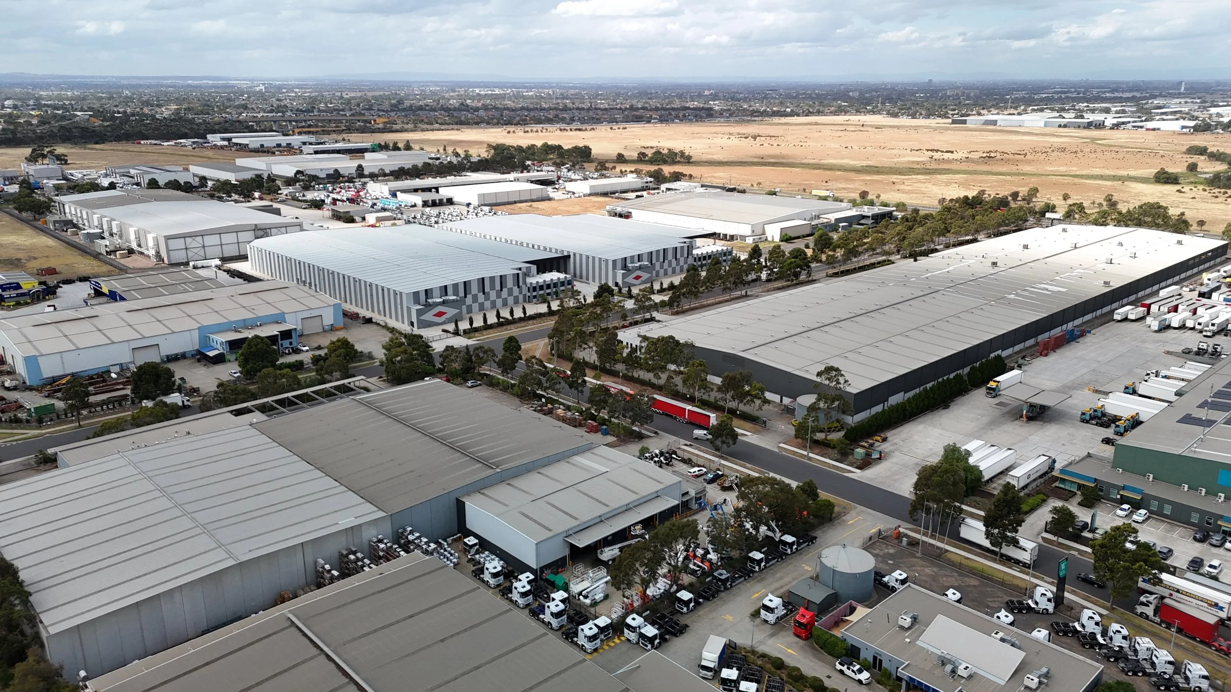 Aerial view of a large industrial warehouse complex with multiple buildings, parking lots, and trucks in a commercial area.