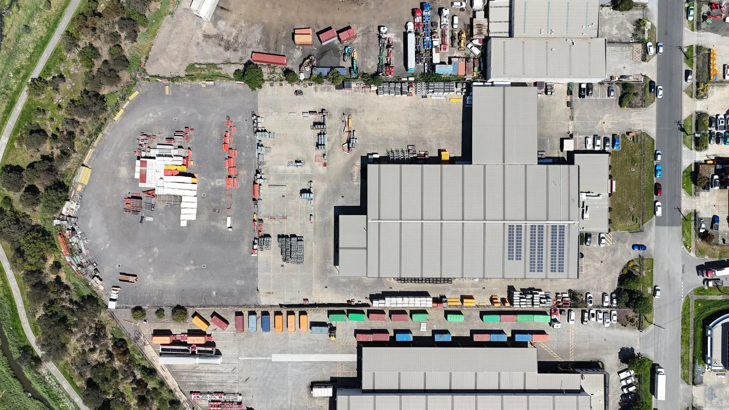 A bird's eye view of a large industrial or warehouse facility with multiple buildings, parking lots, and various colored containers and trucks.