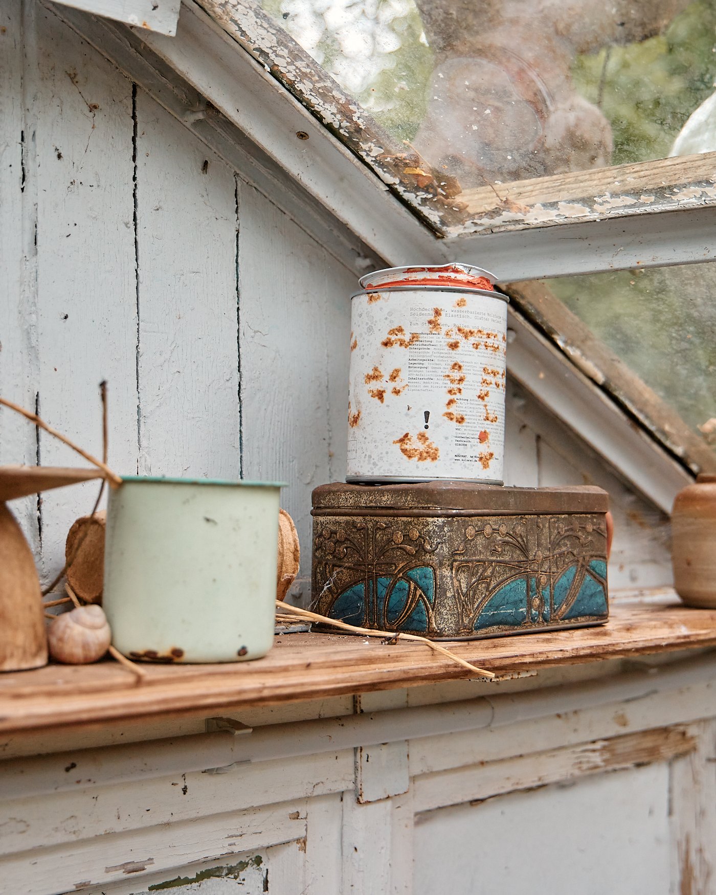 Rusty, weathered tins and small cups arranged on a wooden shelf in a rustic setting.