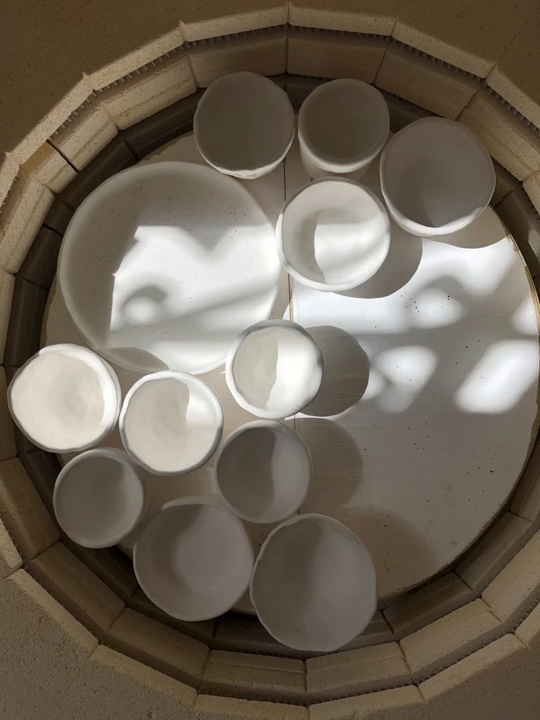 A circular arrangement of white ceramic cups and bowls, with light and shadow creating abstract patterns inside a brick or stone structure.