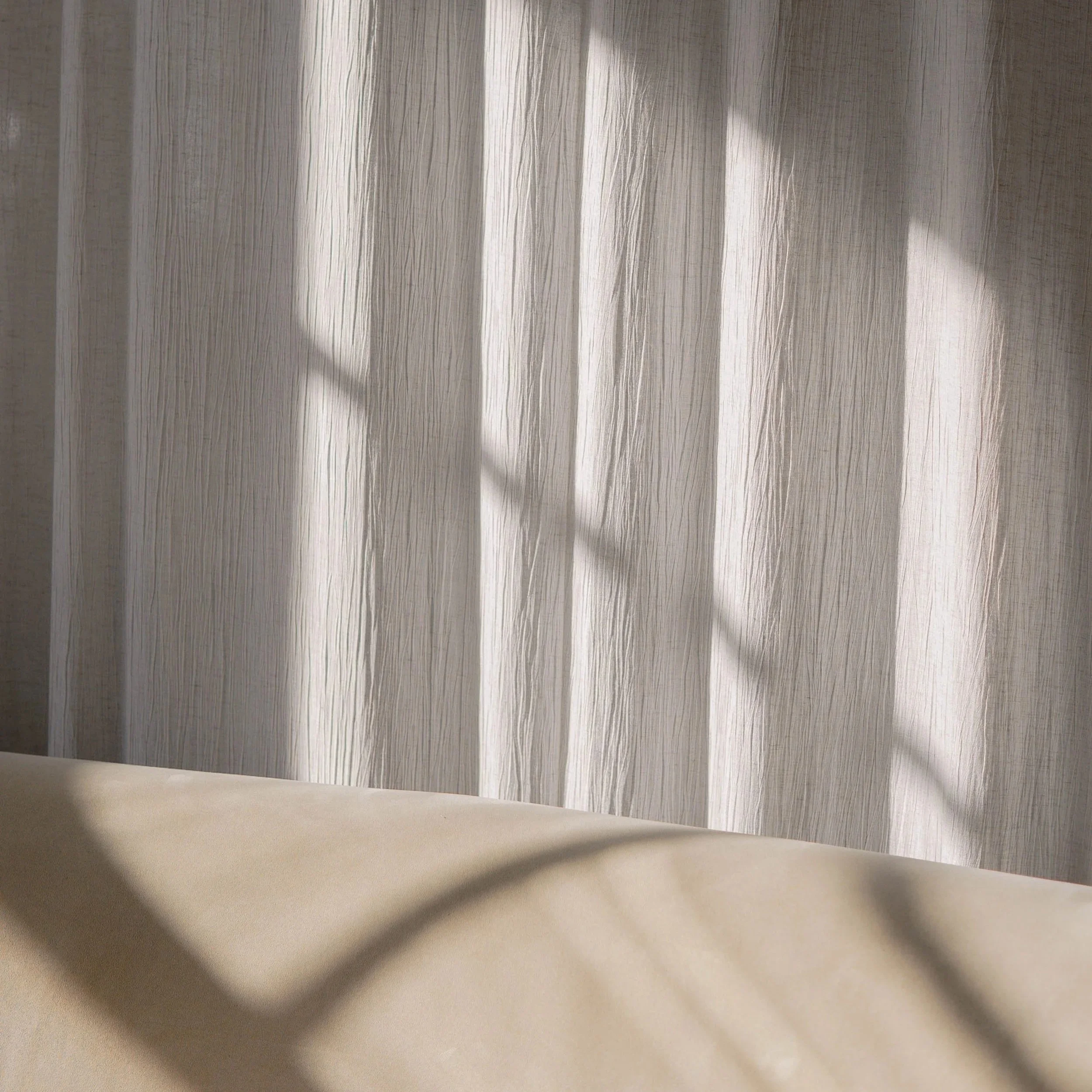 Sunlight casting shadows through window blinds onto a textured beige curtain and a beige surface.