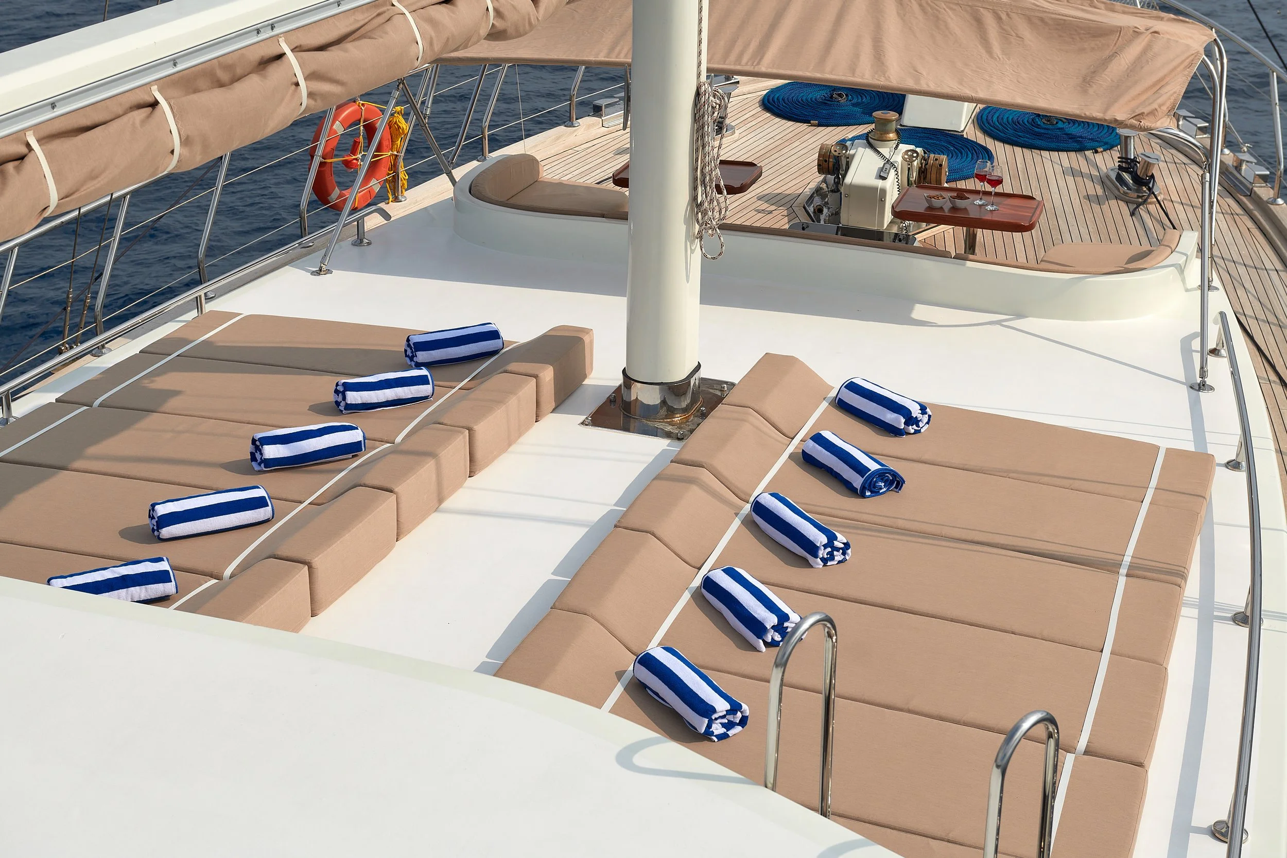 Sunbathing area on a yacht with brown cushioned lounges, blue and white striped towels, and a view of the ocean.