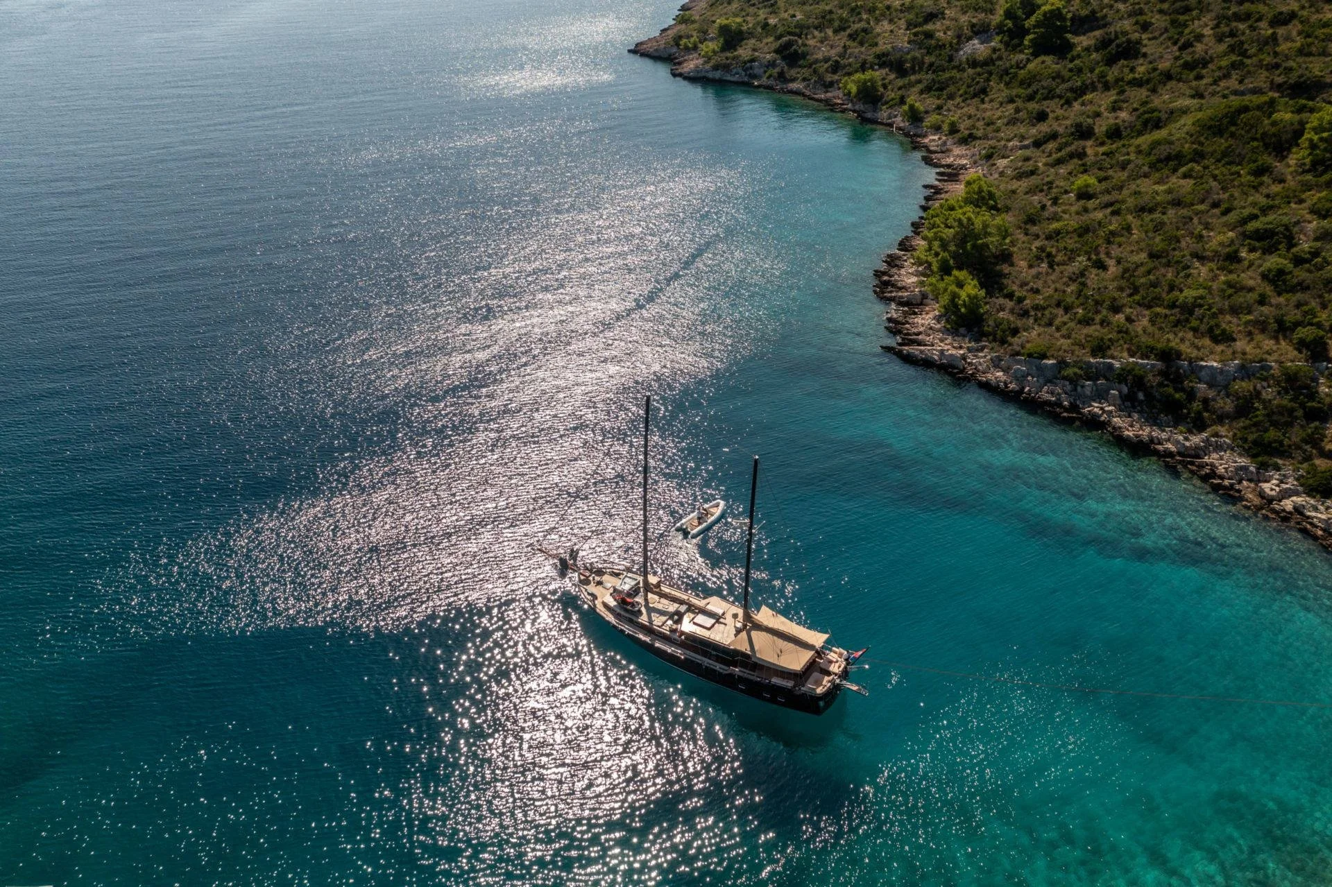 Sailboat on clear blue water near rocky coastline, aerial view