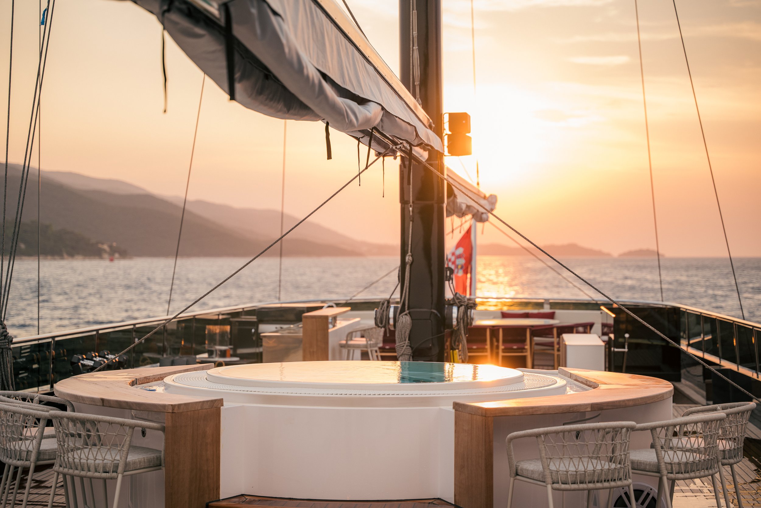 Sundeck of a yacht with a hot tub, sitting area, and view of the ocean at sunset.