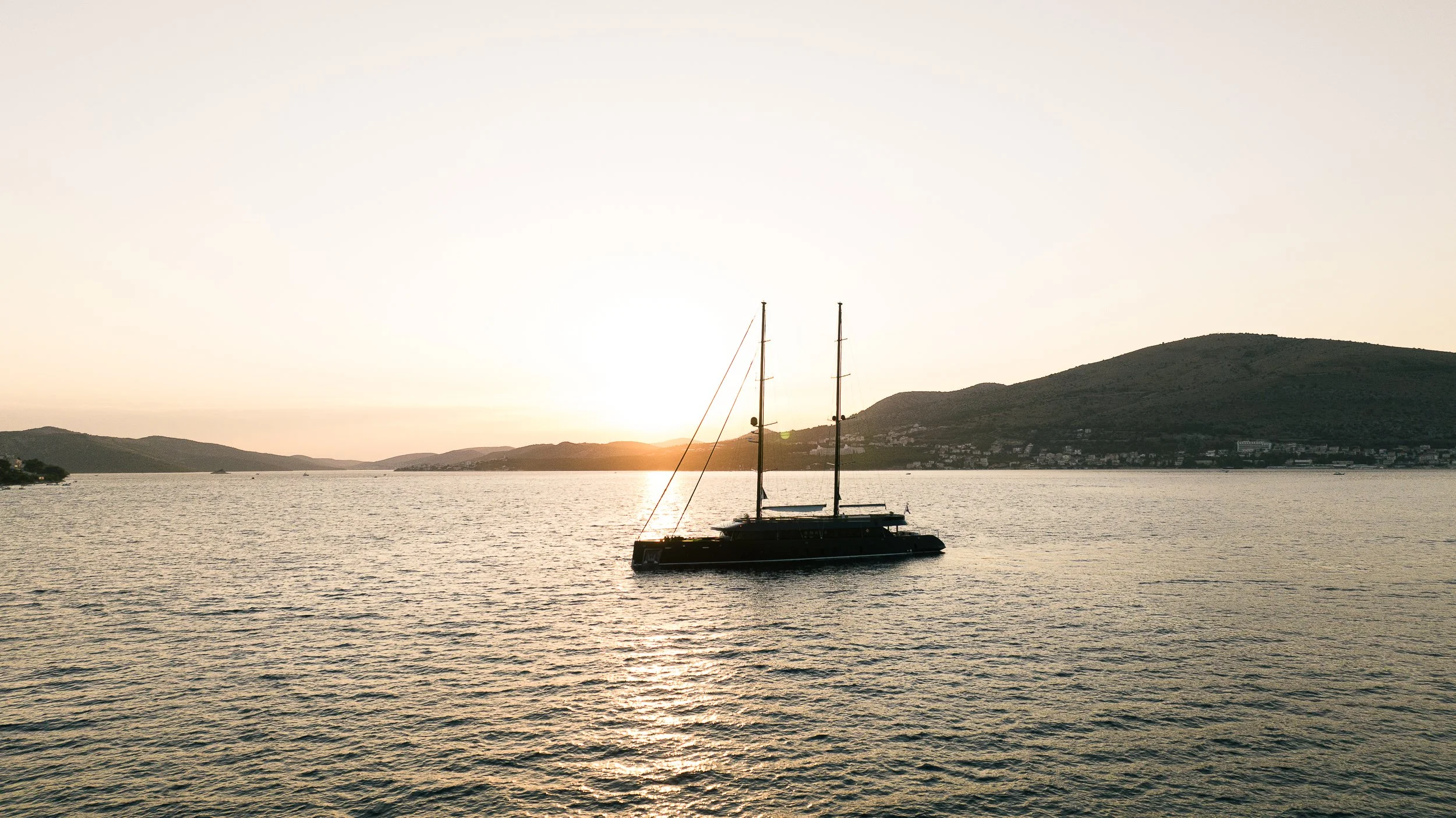 A sailboat on calm water during sunset with hills in the background.