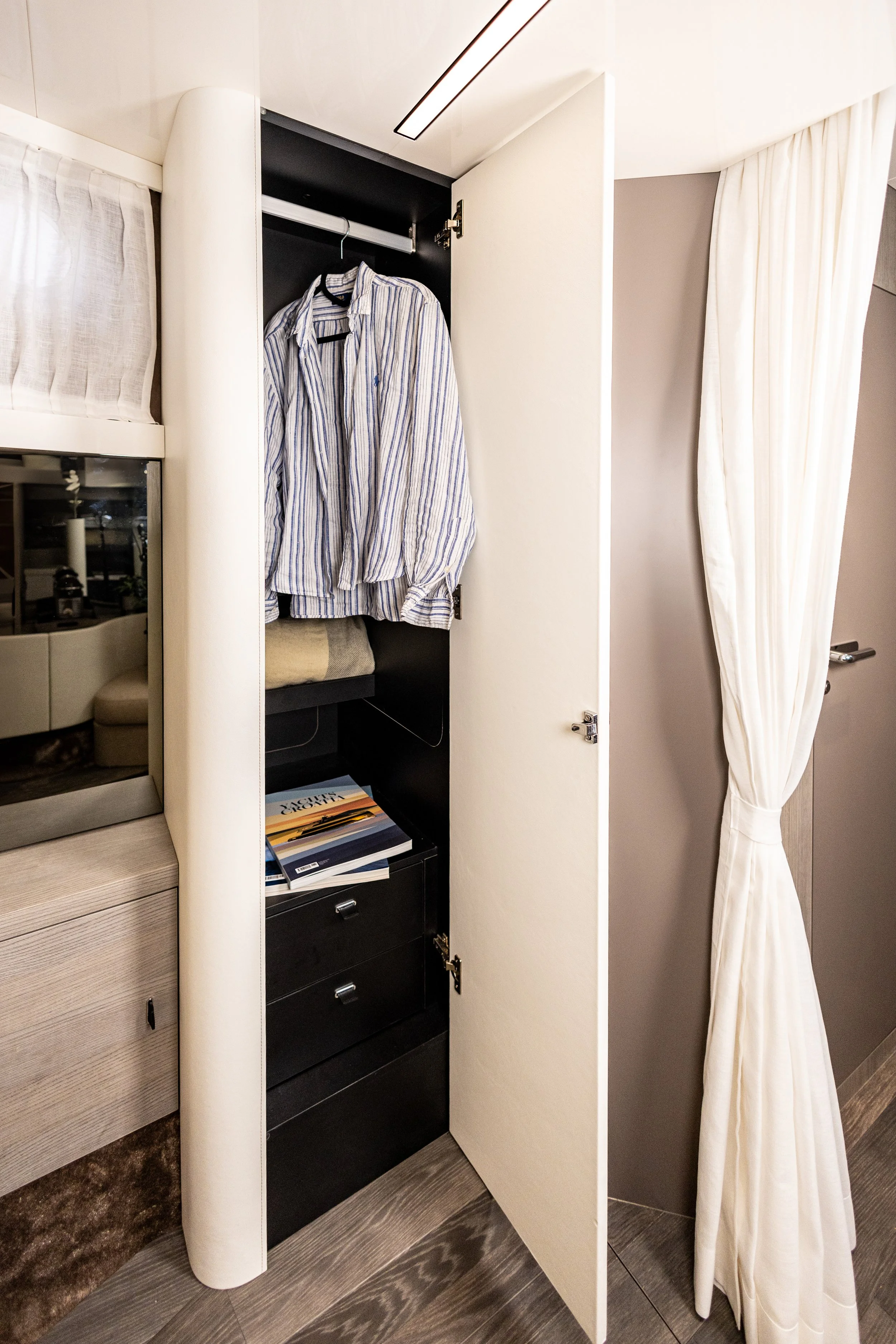 Open hotel closet with a striped shirt hanging inside and books below.