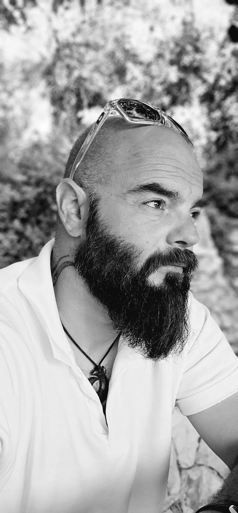 Black and white portrait of a bearded man wearing a white shirt and sunglasses.
