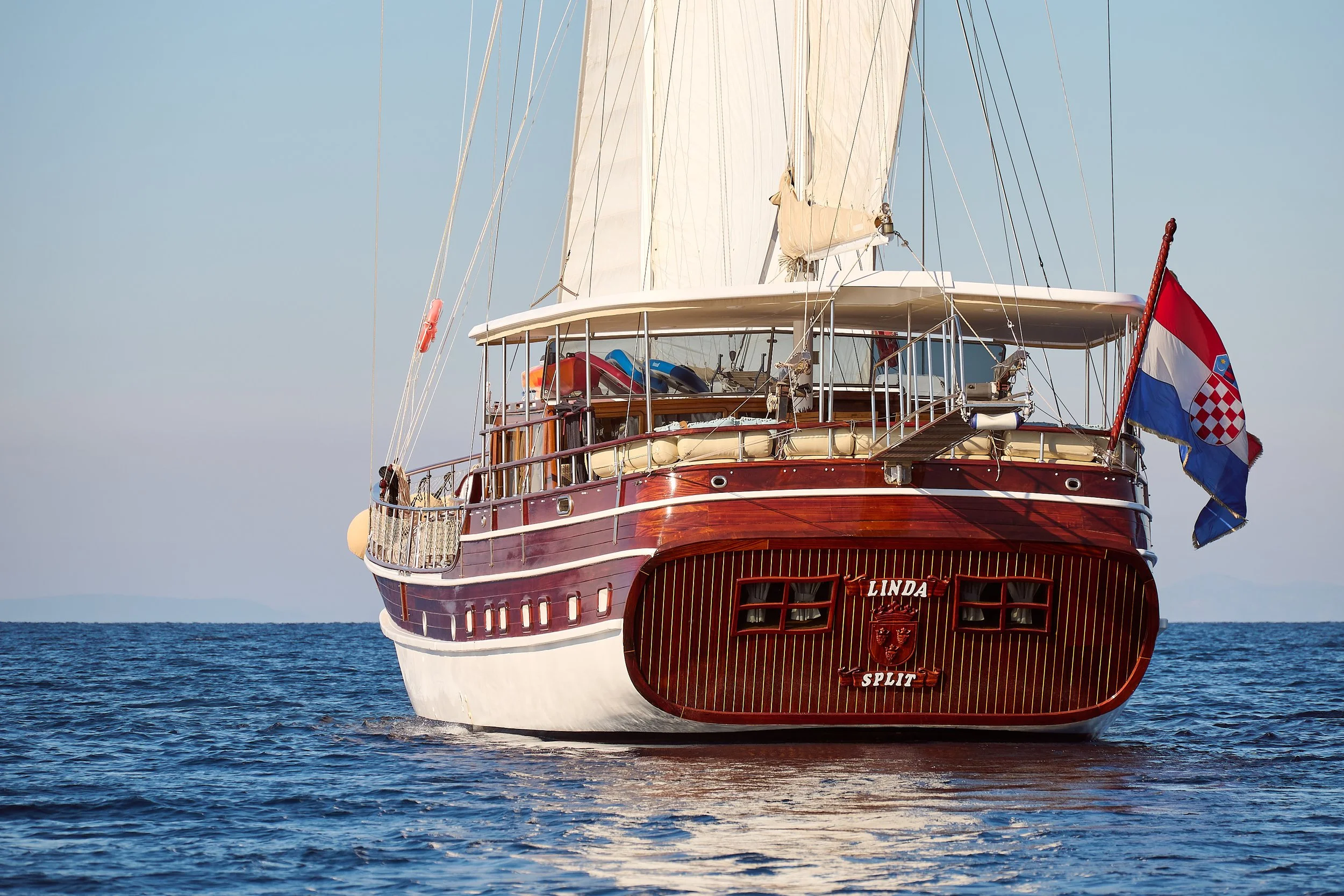 A wooden sailing yacht named 'Linda' sailing on calm blue waters, with Croatian flag flying at the stern.