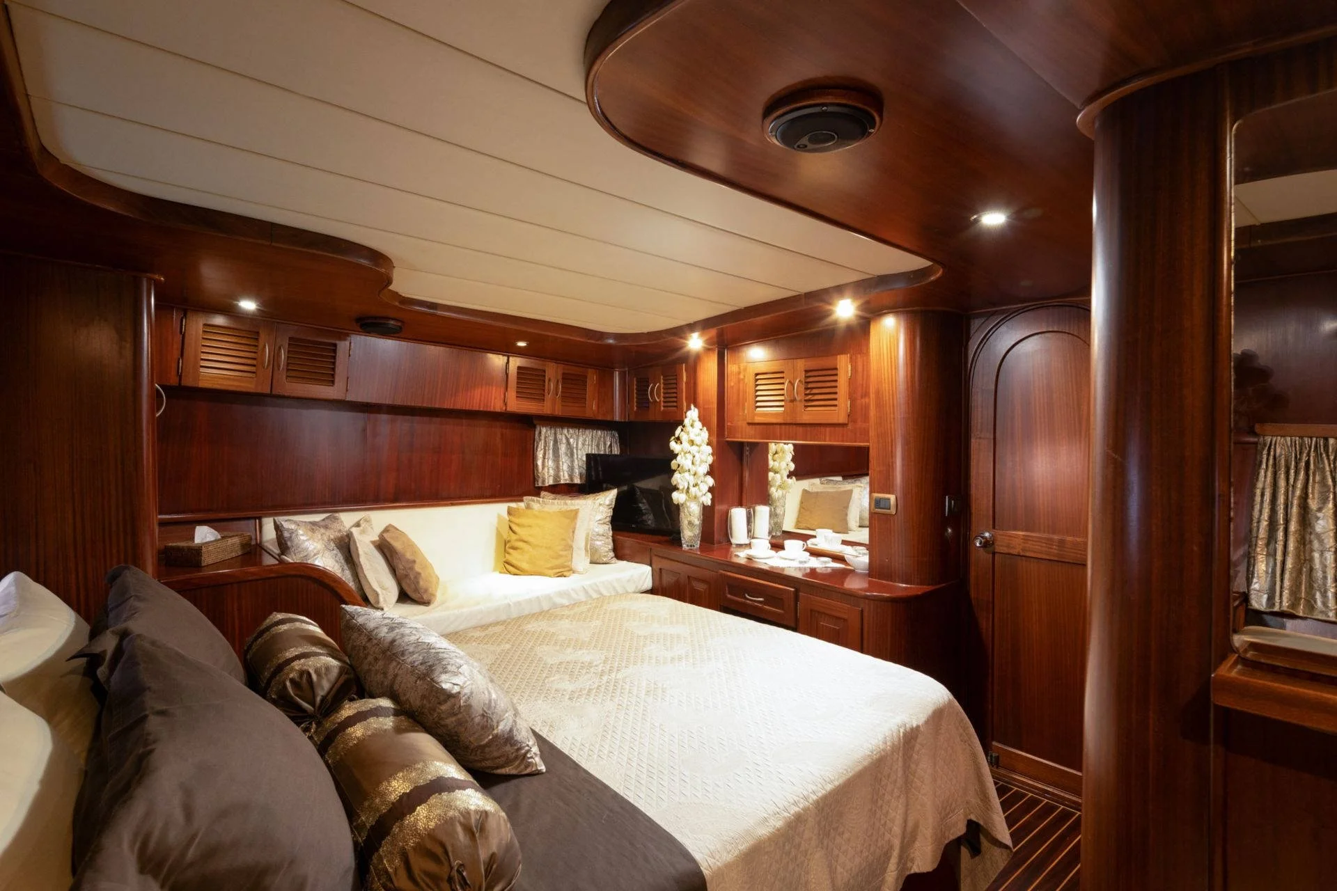Luxurious yacht cabin with wooden paneling, double bed, decorative cushions, bedside table, and soft lighting.