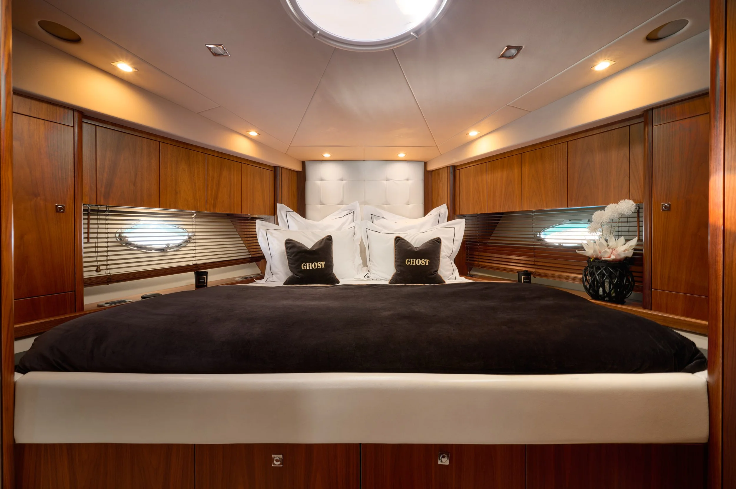 Luxurious bedroom with wooden paneling, white upholstered headboard, and black bedding. Decorative pillows and flowers on a side table.