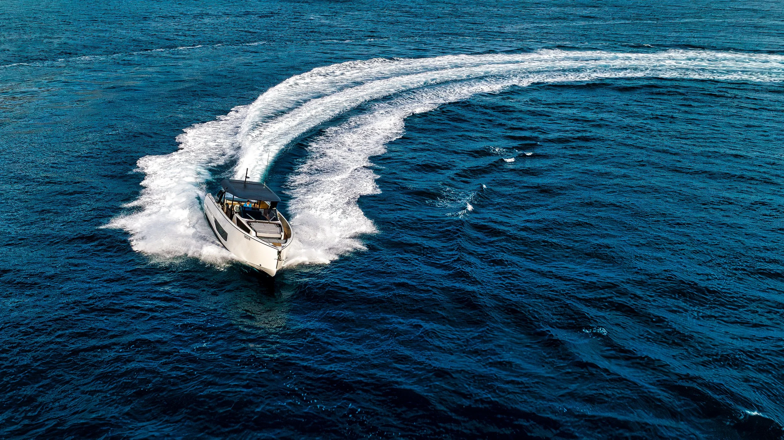 A white motorboat speeding through the deep blue ocean, creating a large wake behind it.