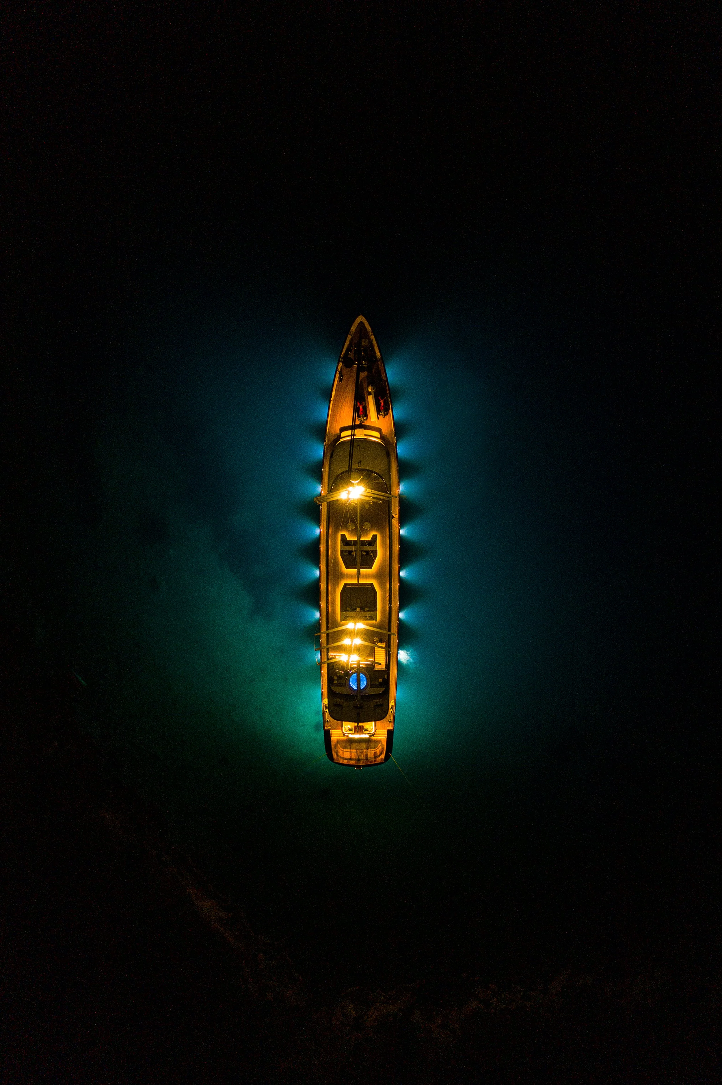 A boat illuminated with lights, viewed from above at night on dark water.