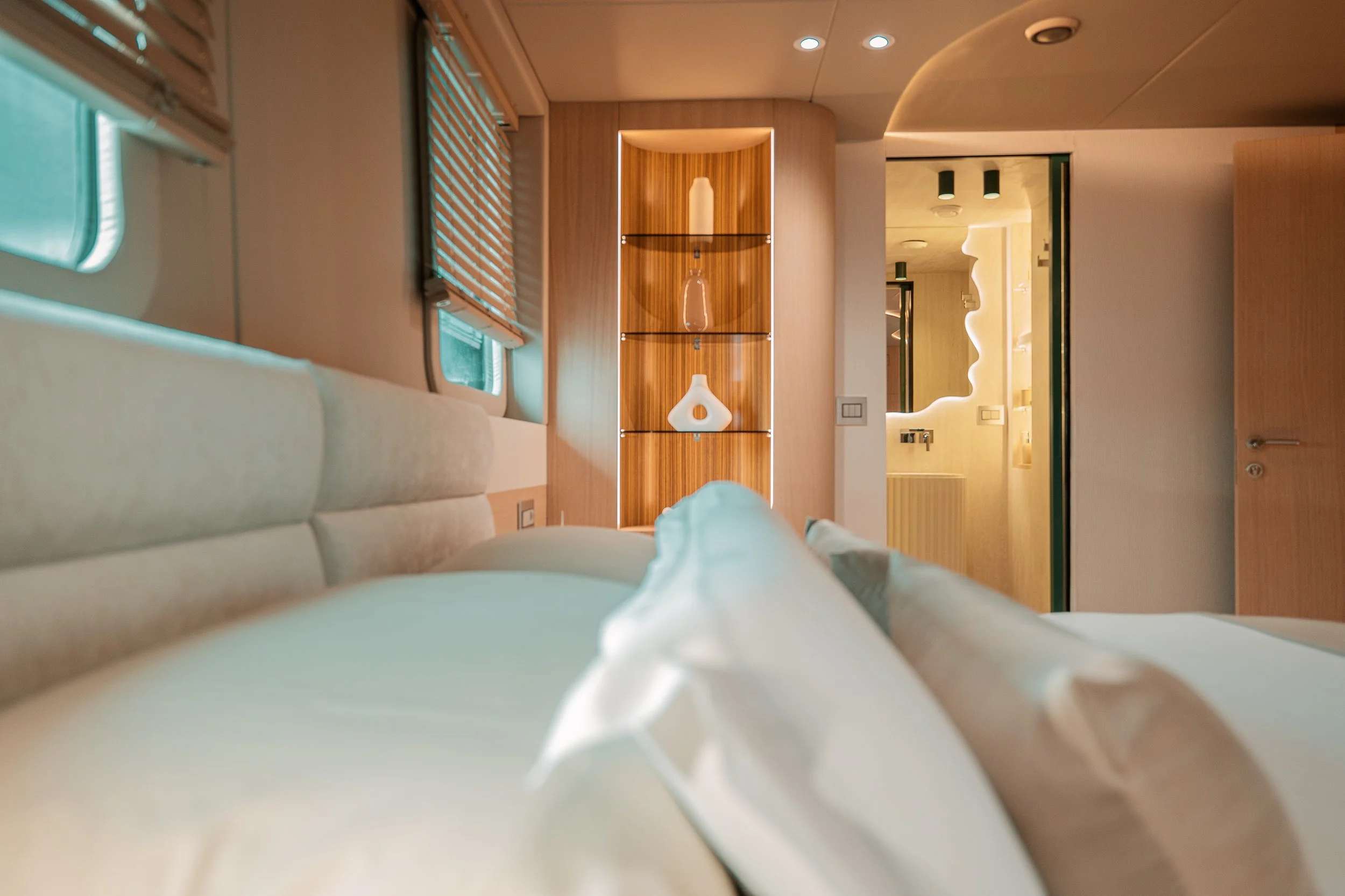 Bedroom with a bed, wooden shelf with decorative vases, and a well-lit bathroom with a face-shaped mirror.