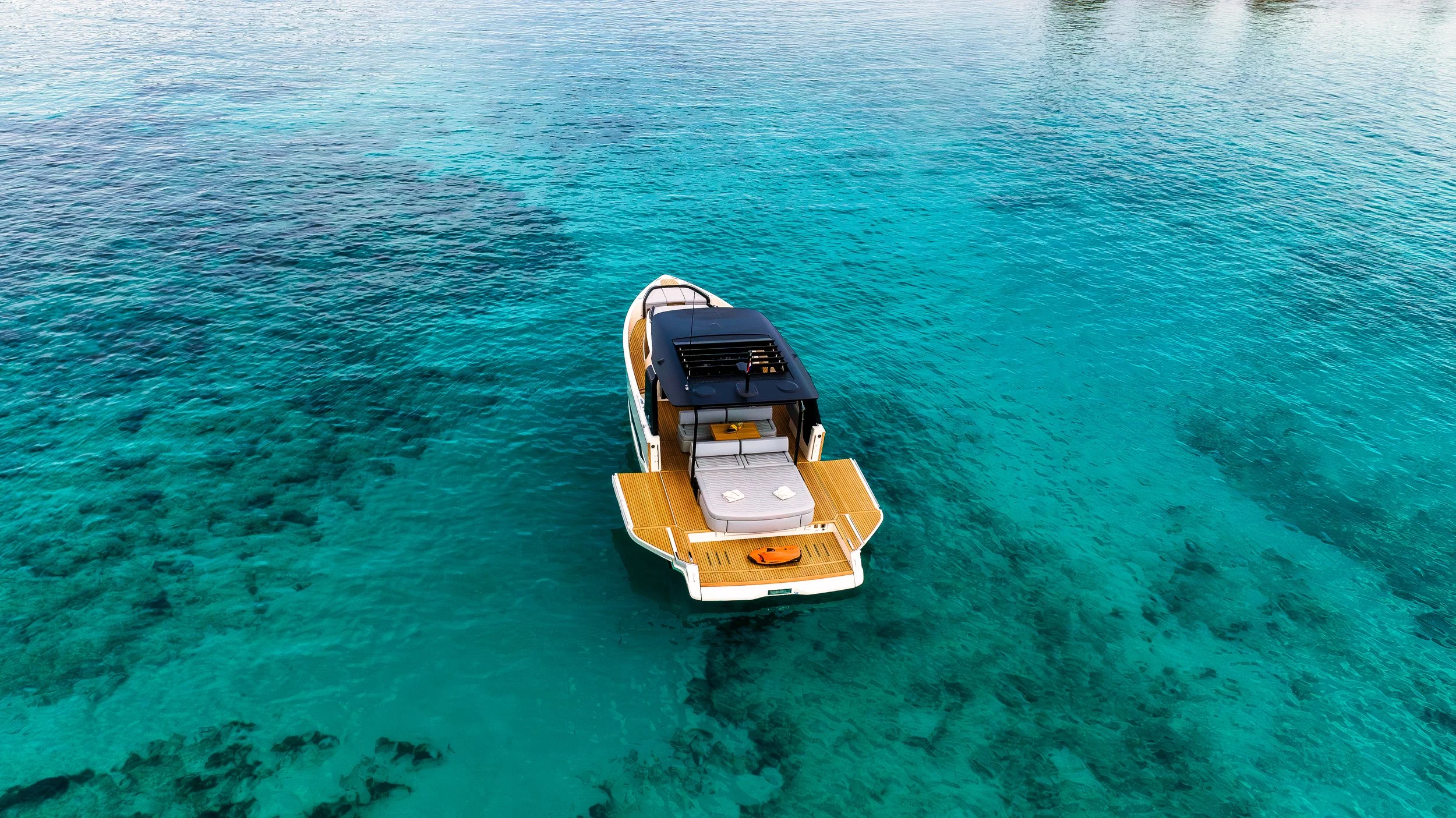 A sleek motor yacht floating on clear blue ocean water with visible coral reefs underneath.