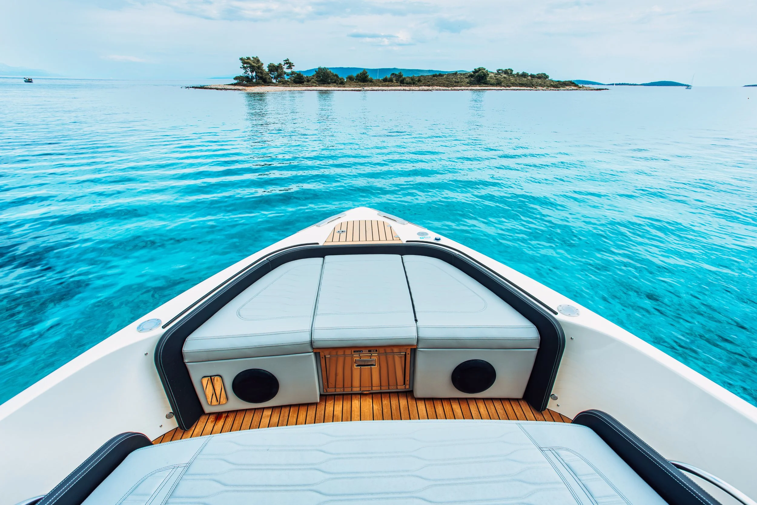 View from the front of a boat looking out at a small island with trees and a calm blue body of water.