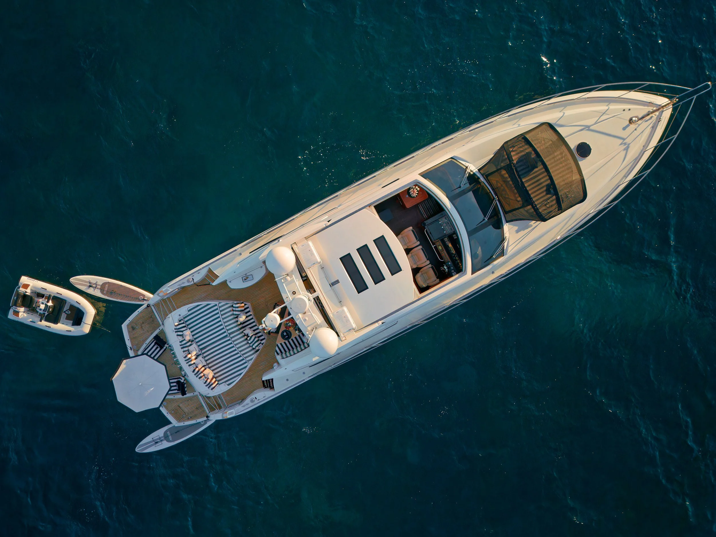 Aerial view of a luxury white yacht with a smaller motorboat nearby on a turquoise ocean, seen from above.