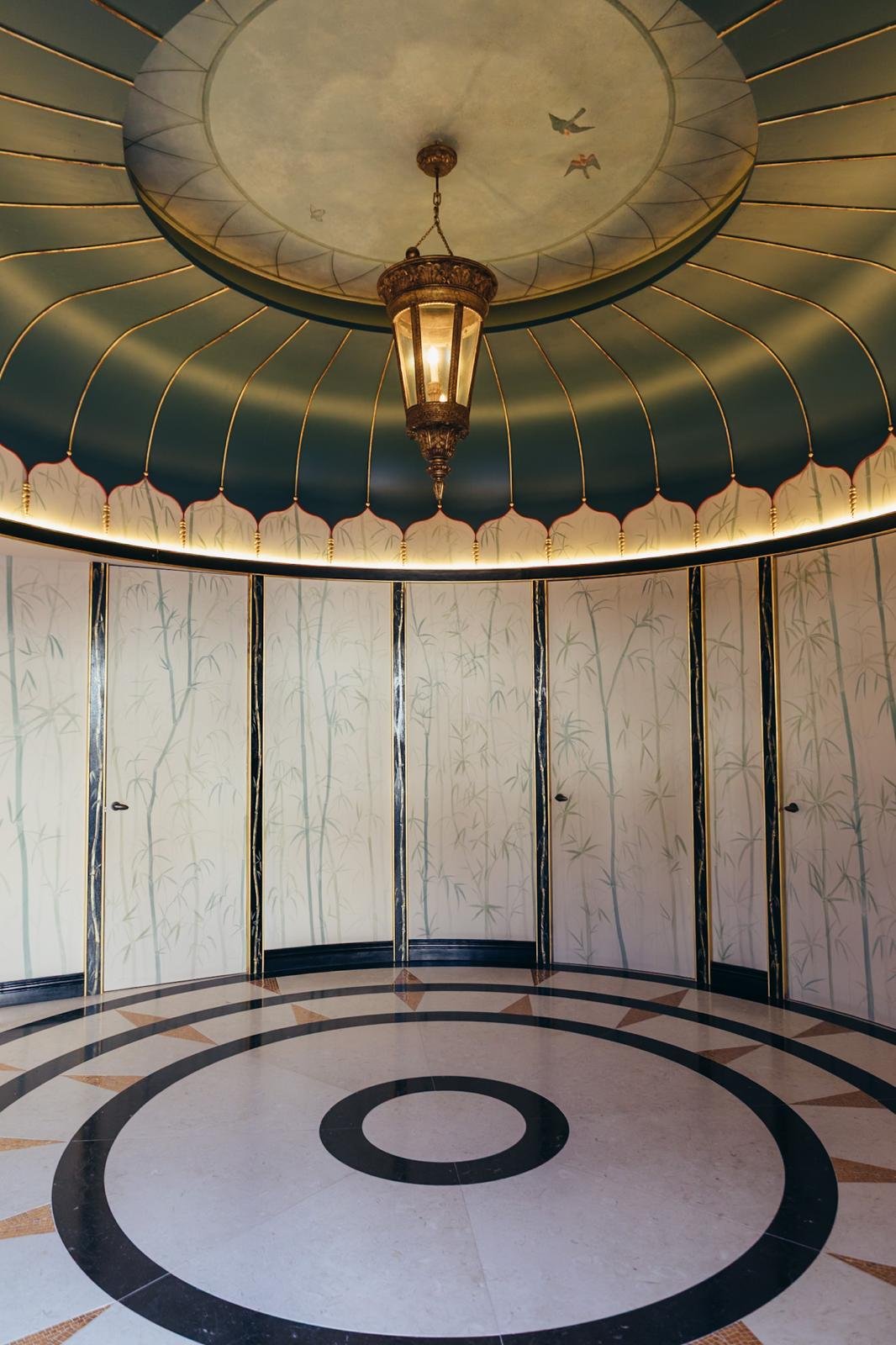 Interior of a circular room with a decorative ceiling, a central chandelier, and wallpaper with bamboo patterns.