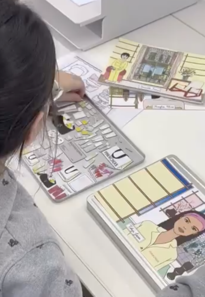 A person working on a collage or craft project with magazines and drawings on a table.