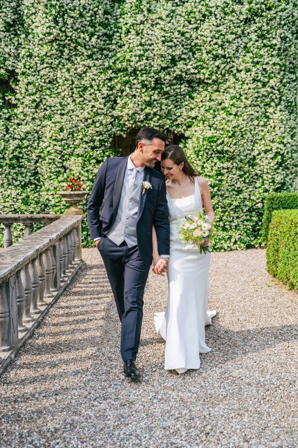 Sposo e sposa felici che si tengono per mano camminando in un giardino fiorito, durante il loro matrimonio.