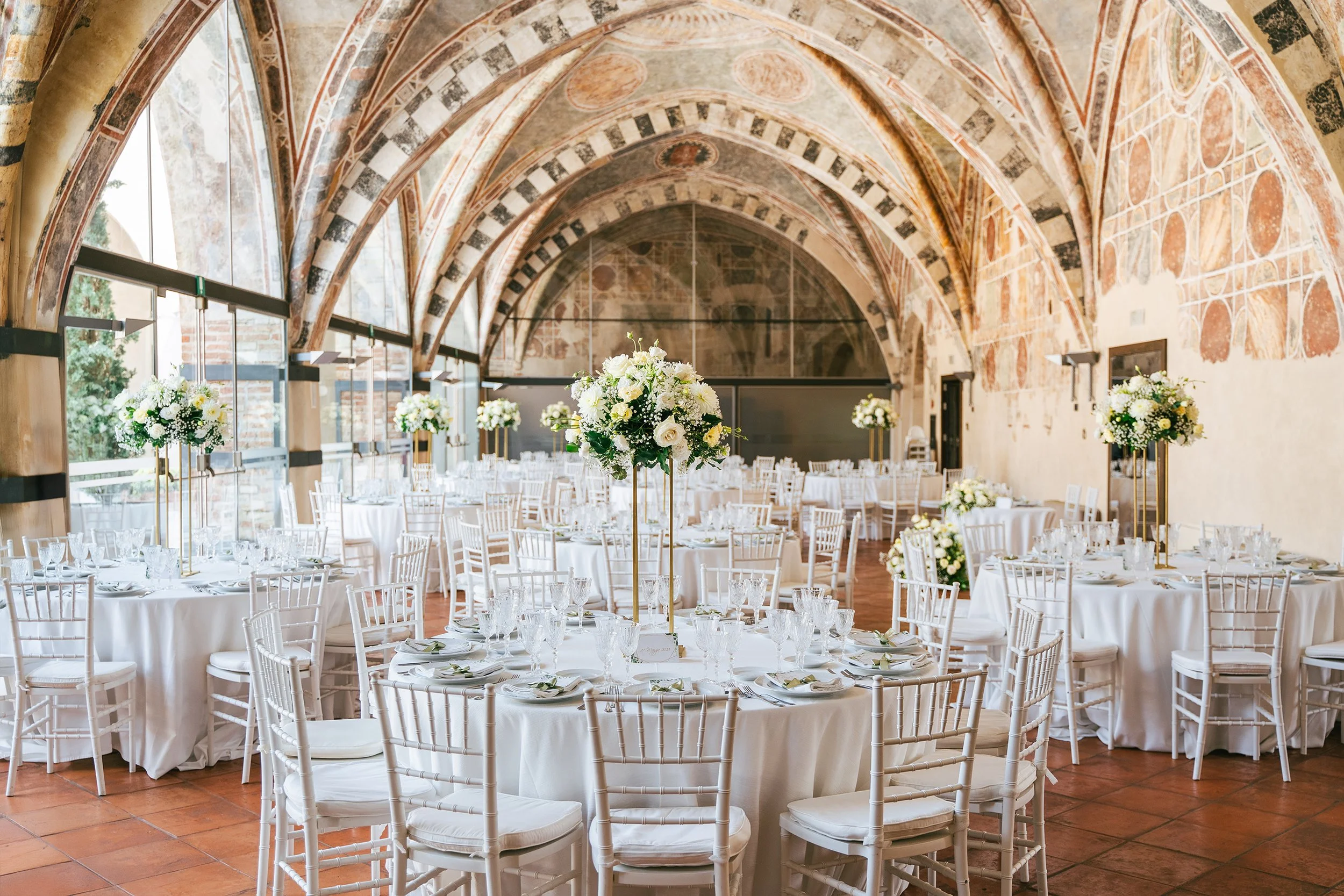 Sala allestita per il ricevimento del matrimonio in un castello i tavoli sono arricchiti da fiori bianchi la sala è tutta affrescata con il soffitto ad archi