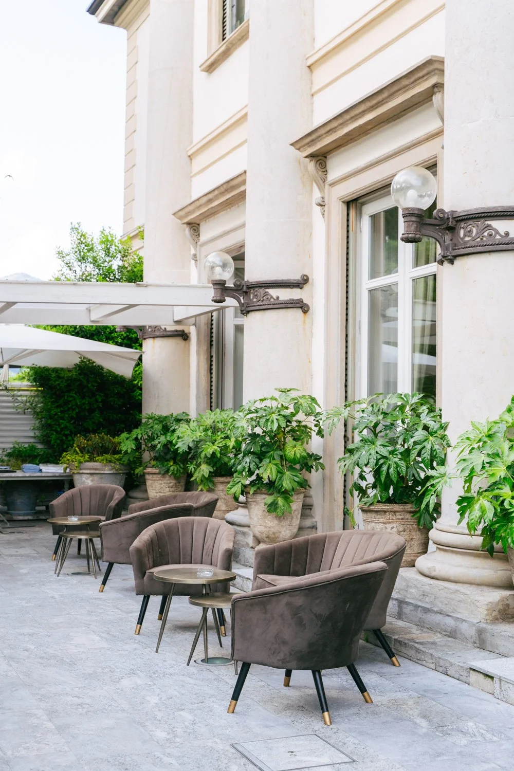 Terrasse con sedie imbottite marroni, tavolini, piante in vaso e uno stabile antico con luci da esterno