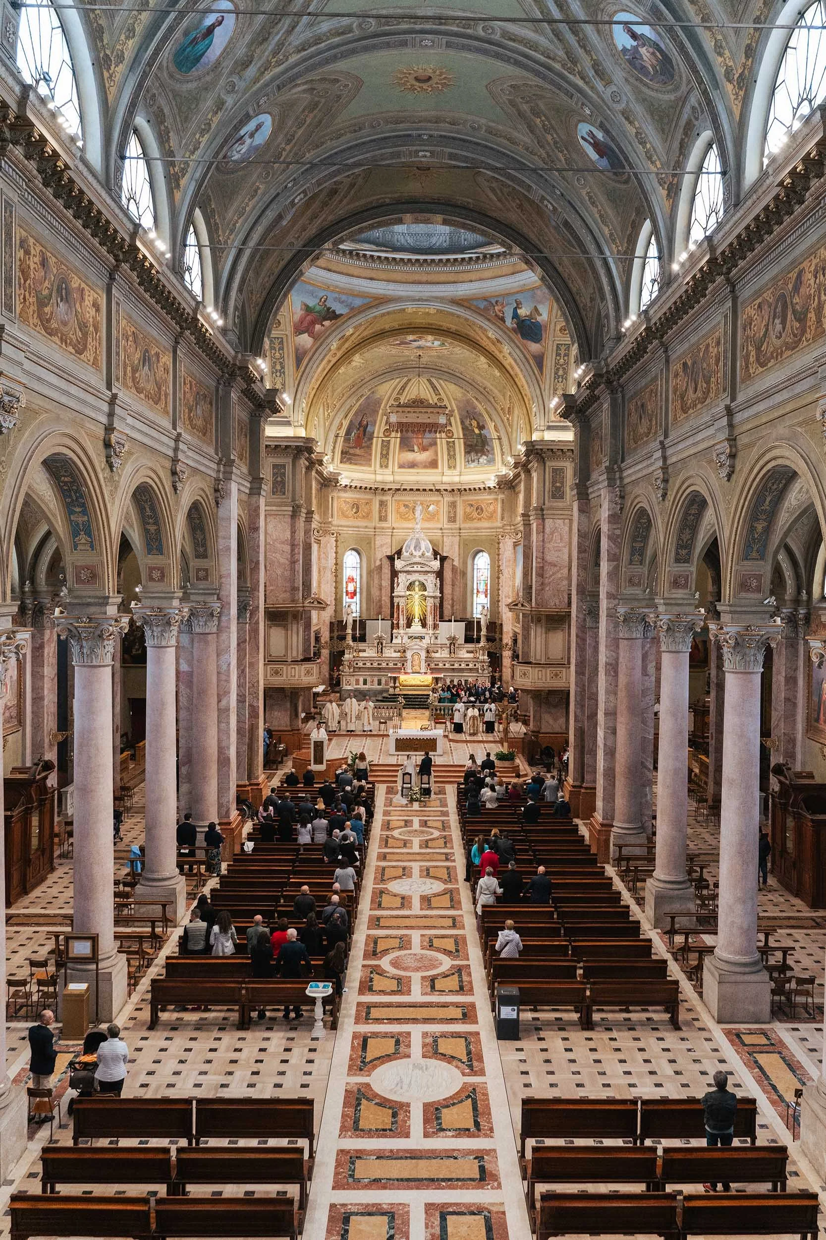 Interno di una chiesa cristiana con archi, colonne e una navata centrale, adoratori e sacerdoti riuniti attorno all'altare.