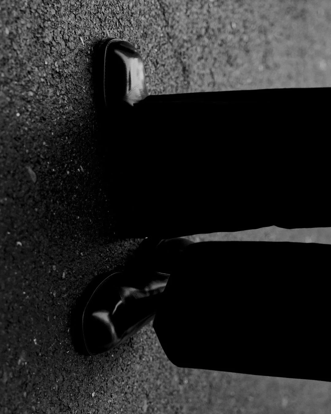 Schwarze Lederschuhe und schwarze Hose stehen auf asphaltiertem Boden.