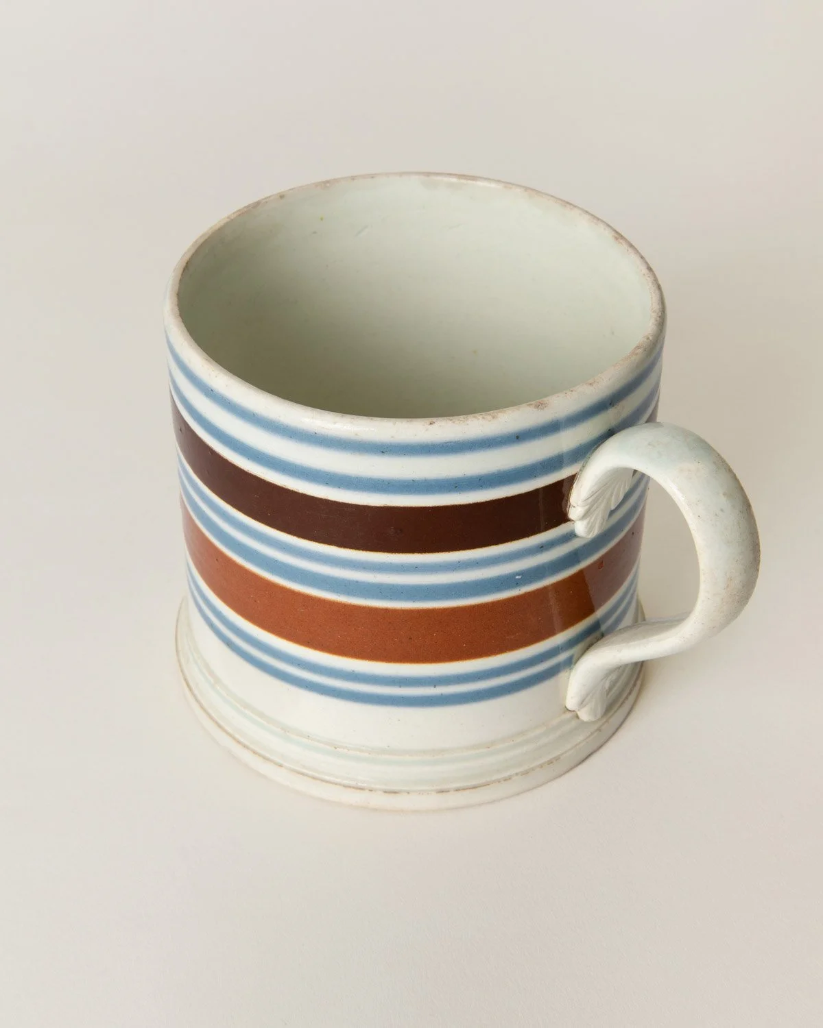 Victorian-era pottery mug with hand-applied bands of blue and brown slip, a molded handle, and traditional craftsmanship.